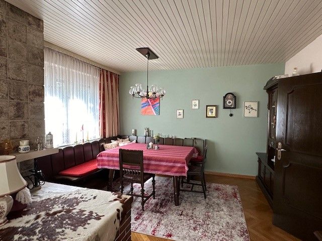 Útulná obývacia izba s jedálenským stolom, rohovou lavicou, kobercom a nástennými hodinami.