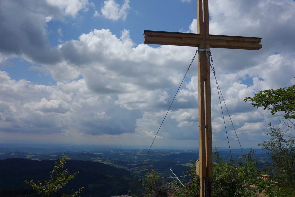 Vrcholový kríž na vyhliadkovej hore Burgsteinmauer s výhľadom na zamračenú oblohu a krajinu.