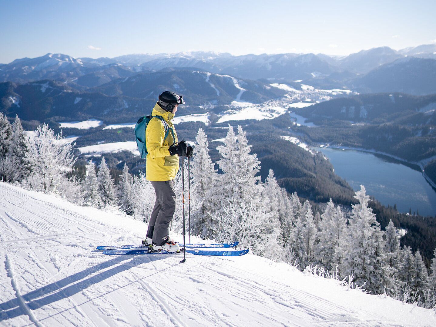 Die strahlende Wintersonne taucht die schneebedeckte Landschaft in ein magisches Licht. Ein Skifahrer genießt den atemberaubenden Ausblick auf die verschneiten Berge und das glitzernde Tal, während die frische, klare Luft die Sinne belebt. Hier, wo die Natur in ihrer reinsten Form erstrahlt, wird jeder Moment zum unvergesslichen Erlebnis.