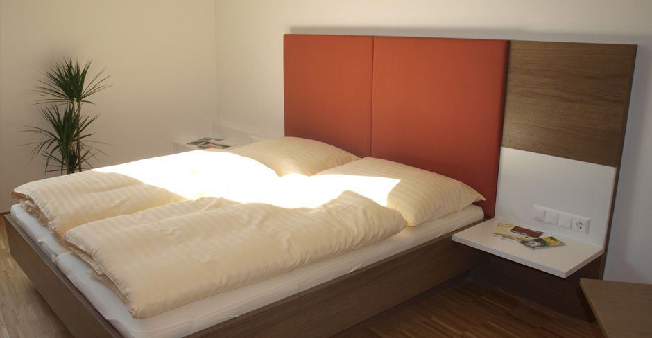 Moderná izba pre hostí s manželskou posteľou, červeným čelom a rastlinami.