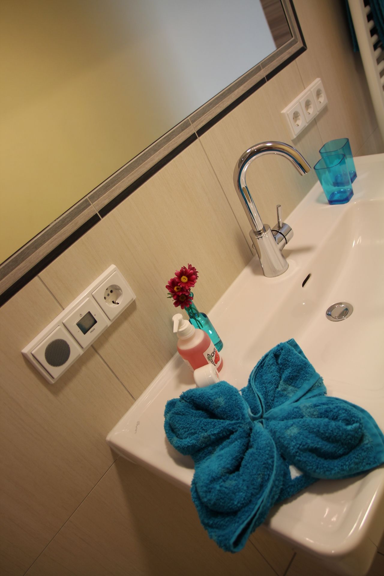 Umývadlo s modrým uterákom, dávkovačom mydla a vázou s kvetmi.