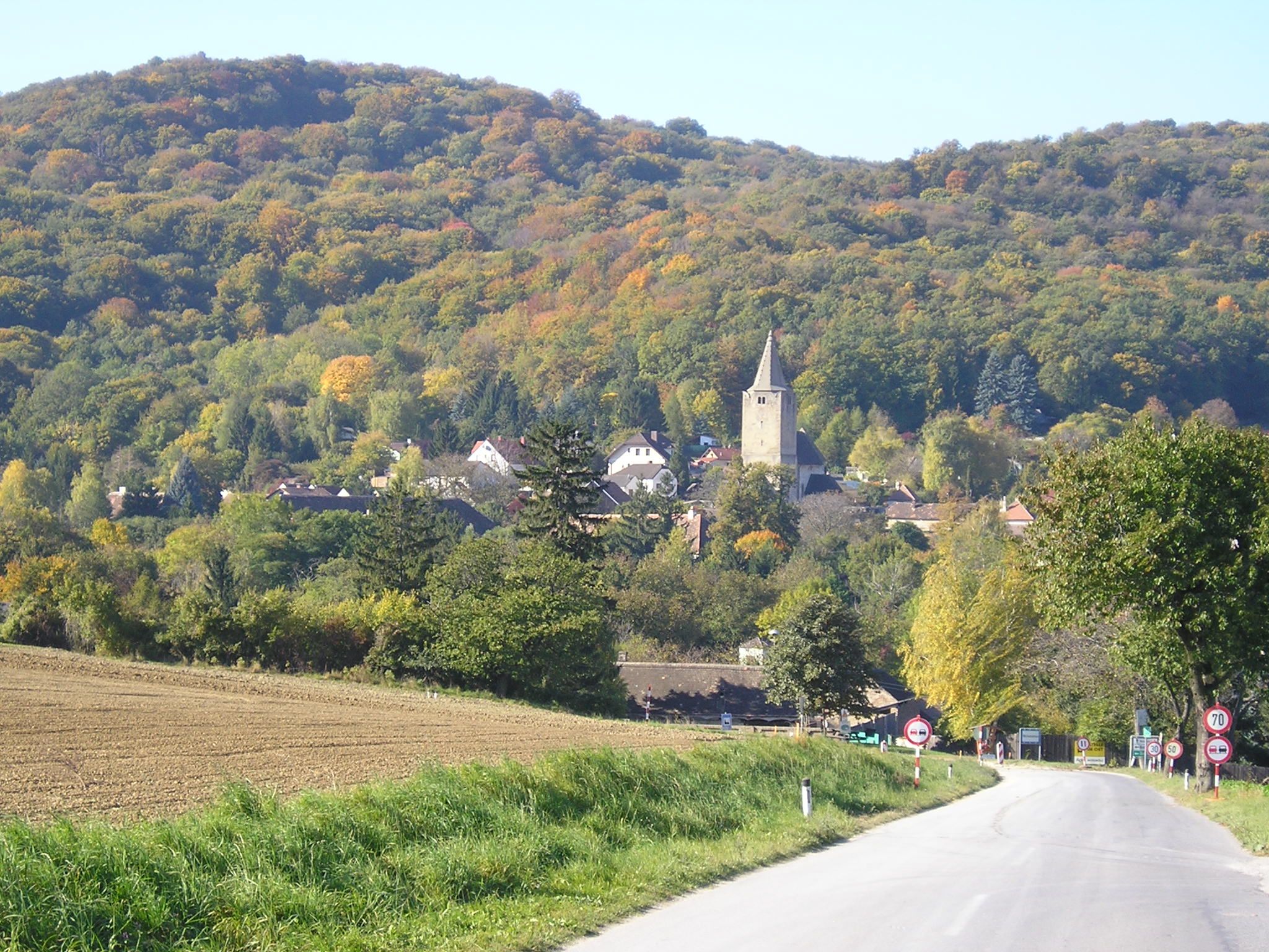 Malebná krajina s cestou vedúcou do dediny s kostolom, obklopená zalesnenými kopcami na jeseň.