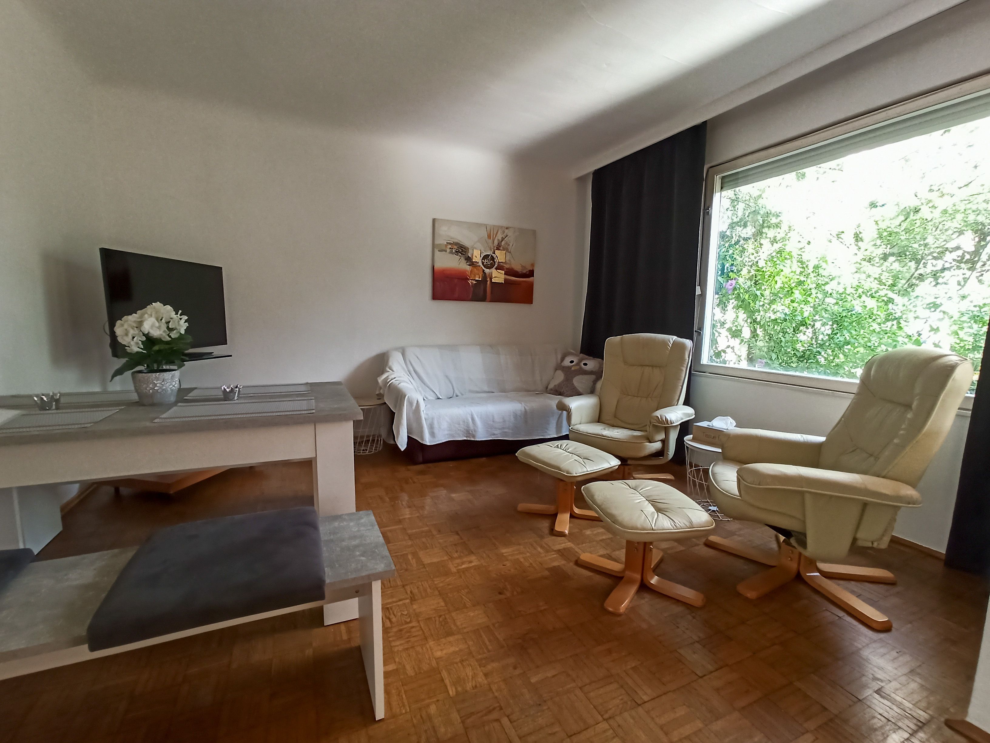 Obývacia izba s pohovkou, dvoma kreslami, stolom a veľkým oknom.