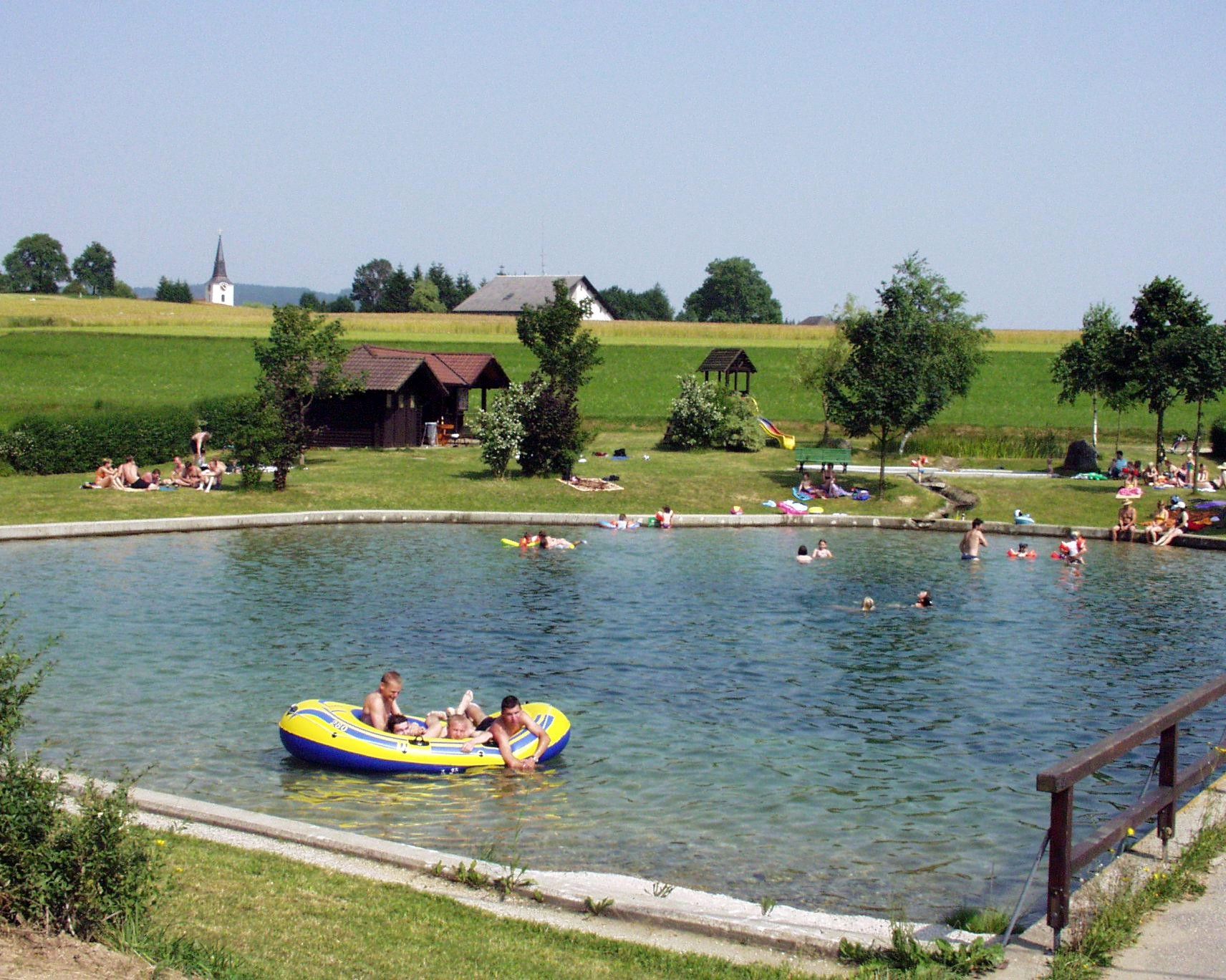 Ľudia sa kúpu v rybníku s okolitou lúkou a stromami.