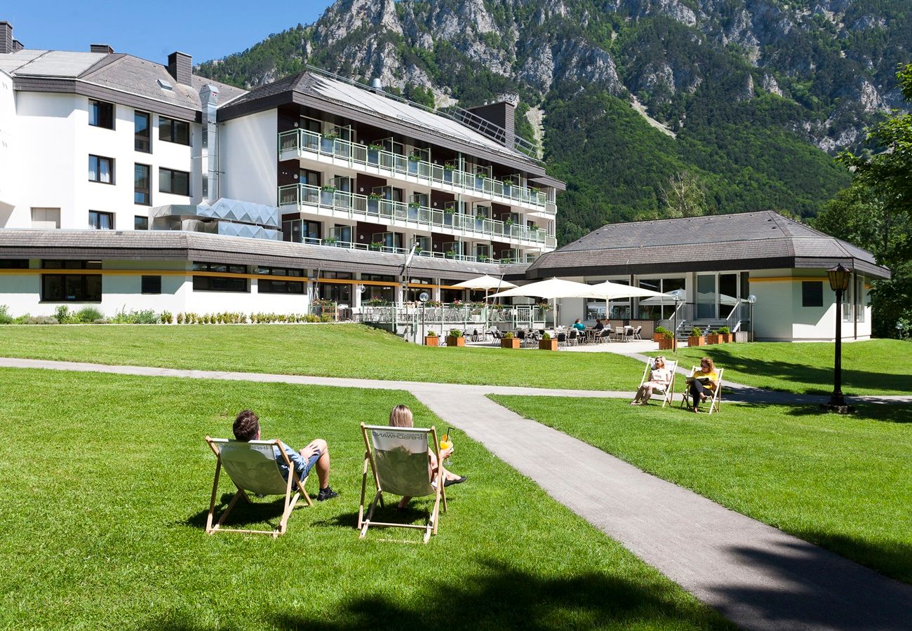 Hotel s terasou a ležadlami na lúke obklopenej horami.