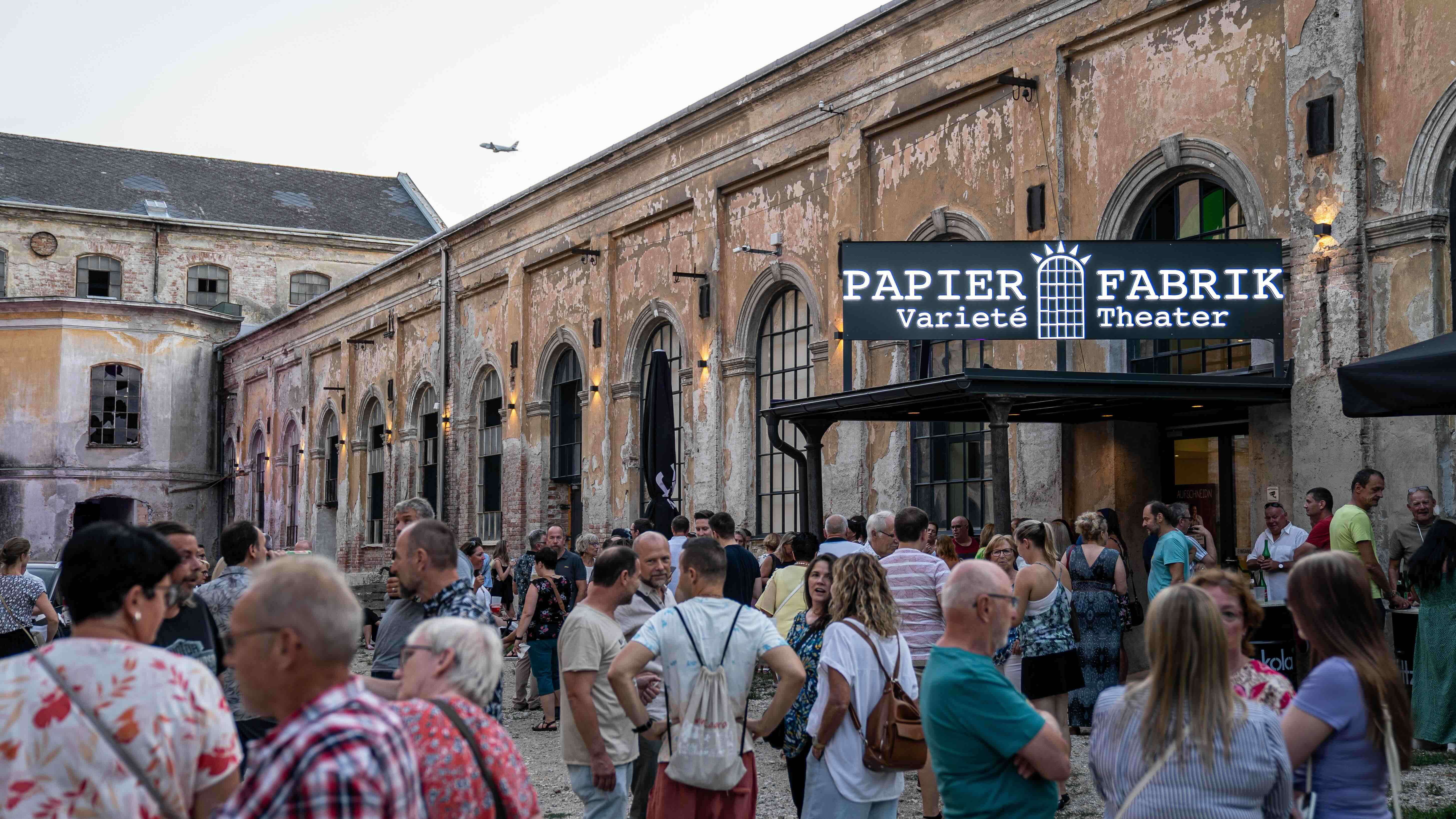 Dav pred starou továrňou na papier s nápisom "Papier Fabrik Varieté Theater".