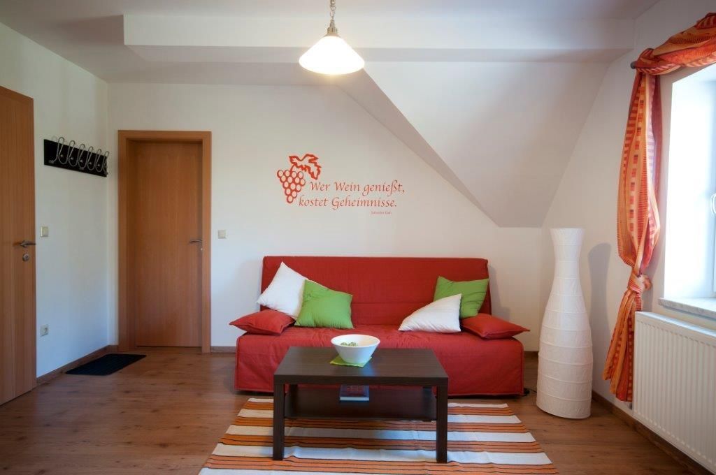 Útulná izba pre hostí s červenou pohovkou, vankúšmi, lampou a nástenným citátom.