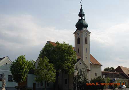 Kostol v Moosbrunne so zelenou kostolnou vežou a okolitými budovami.