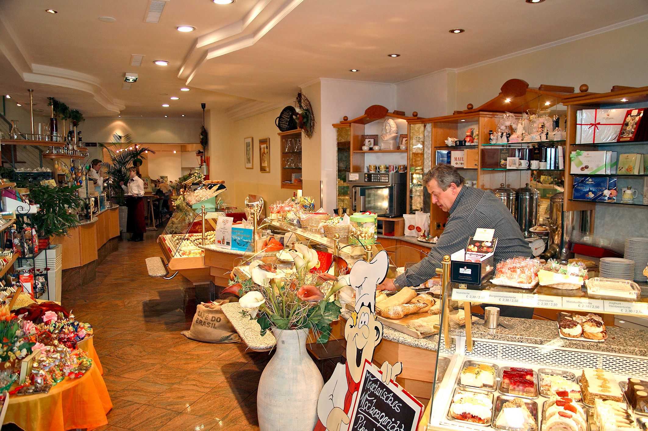 Pohľad do interiéru útulnej kaviarne s pultom plným koláčov a zákuskov.