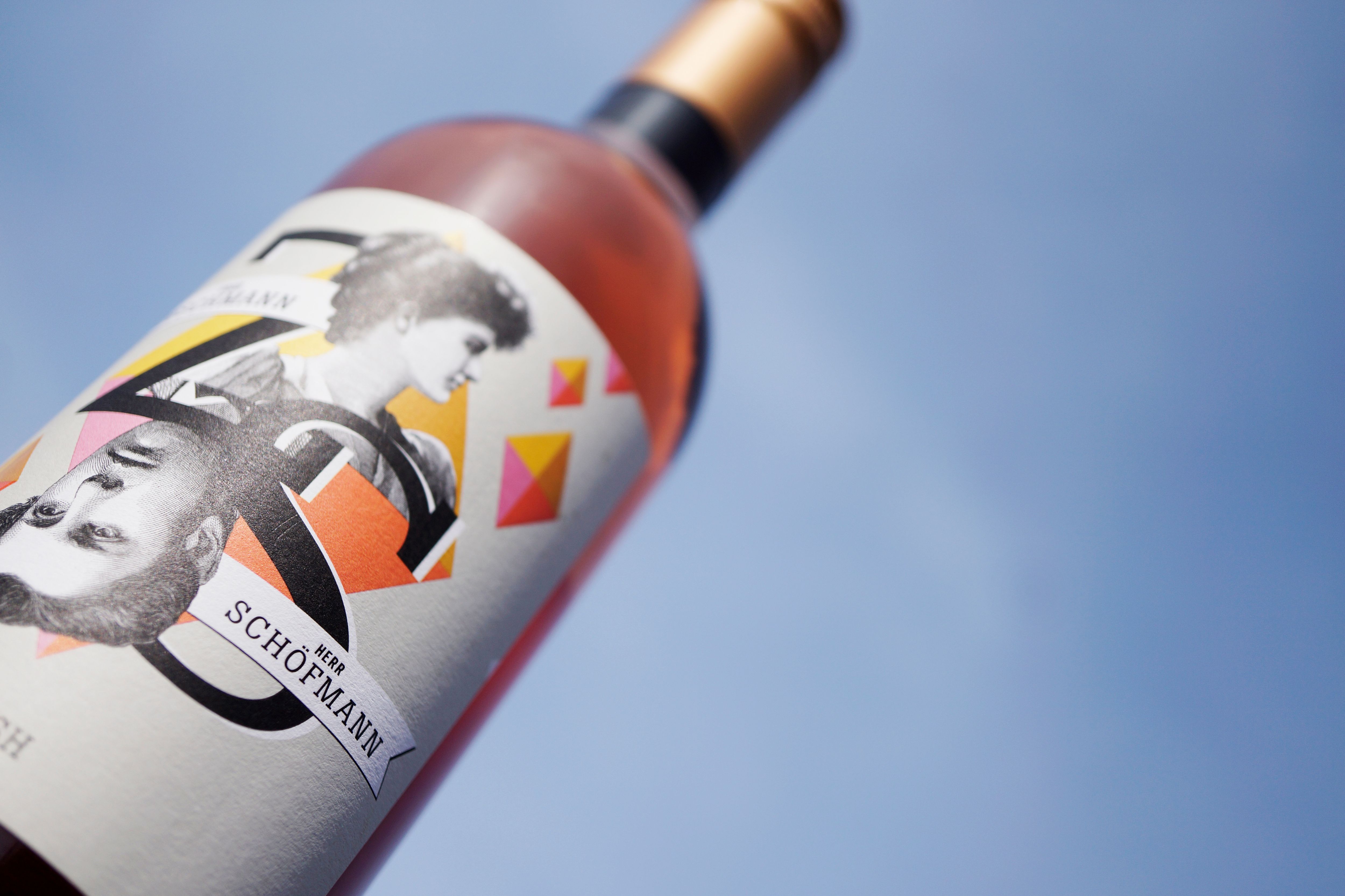 Detailný záber na fľašu vína s umeleckou etiketou na pozadí modrej oblohy.