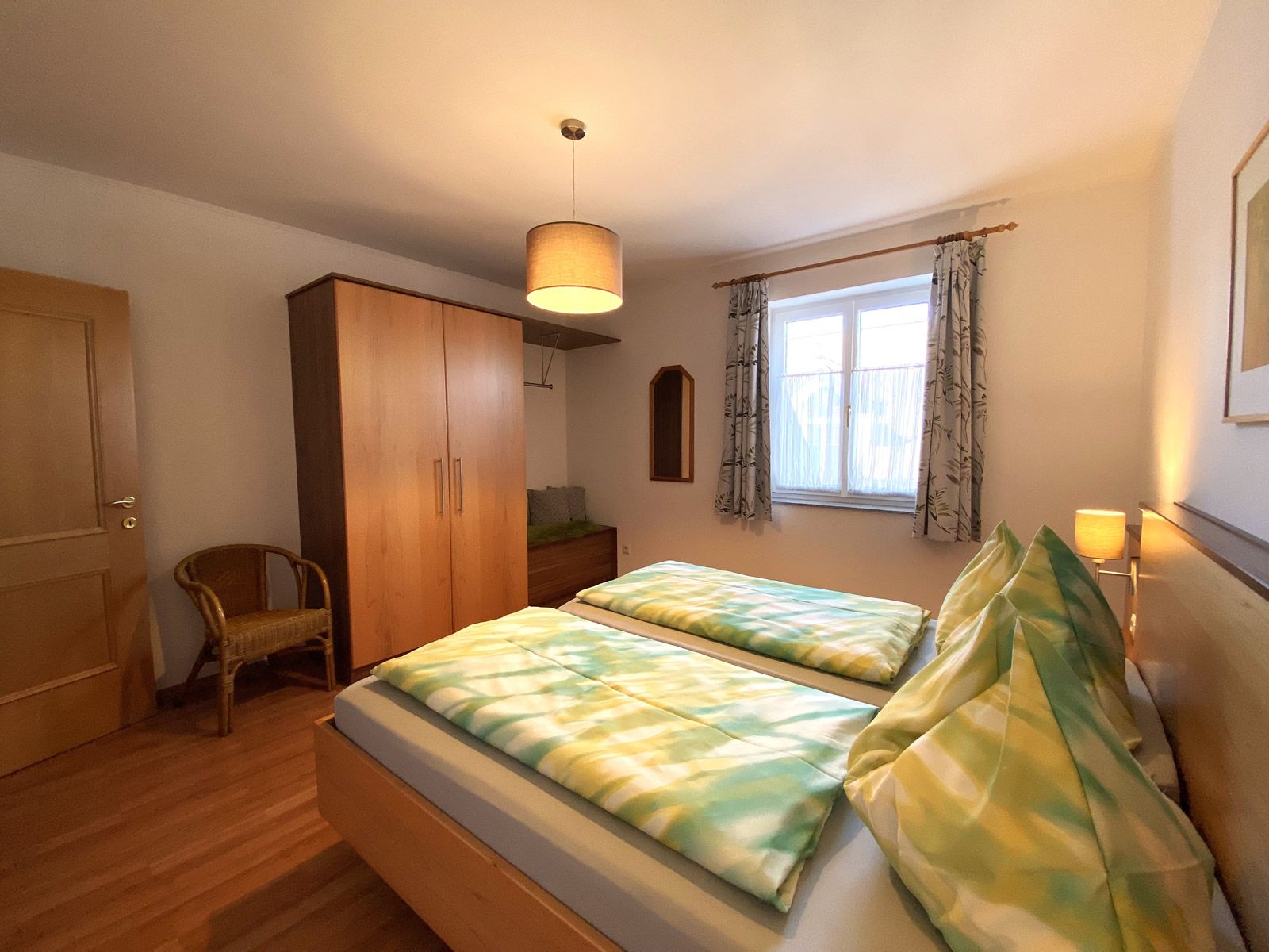 Spálňa s manželskou posteľou, šatníkovou skriňou, stoličkou a oknom.