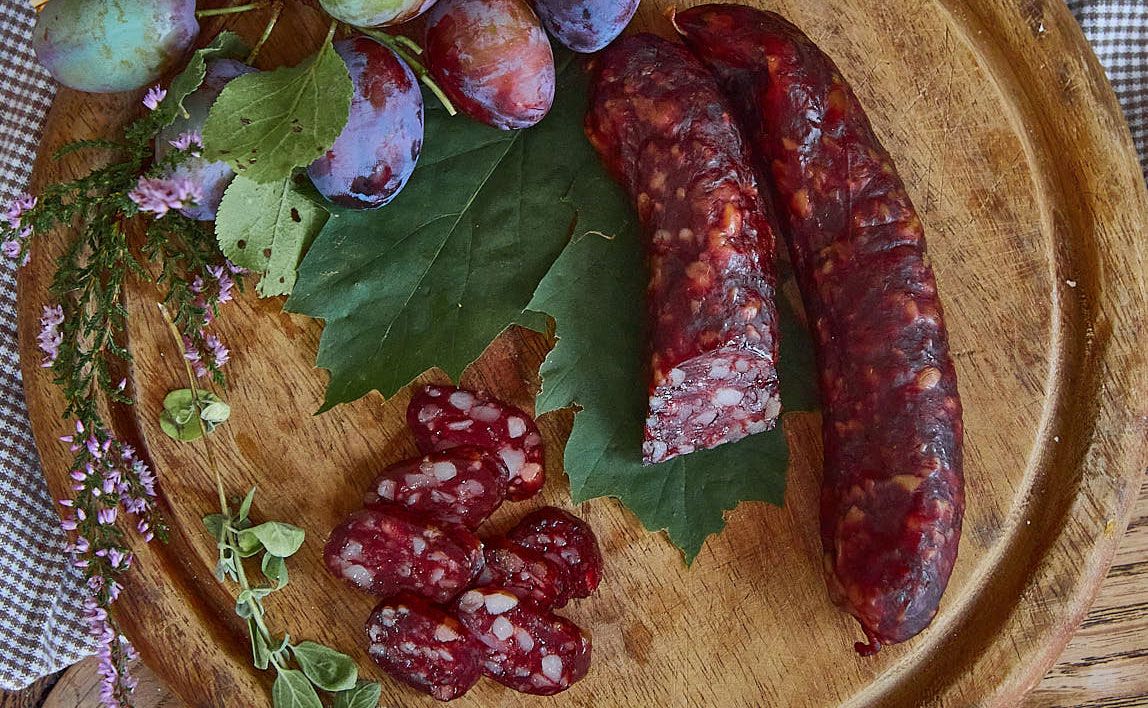 Kaminwurzn a slivky na drevenej doske zdobenej zelenými listami a bylinkami.