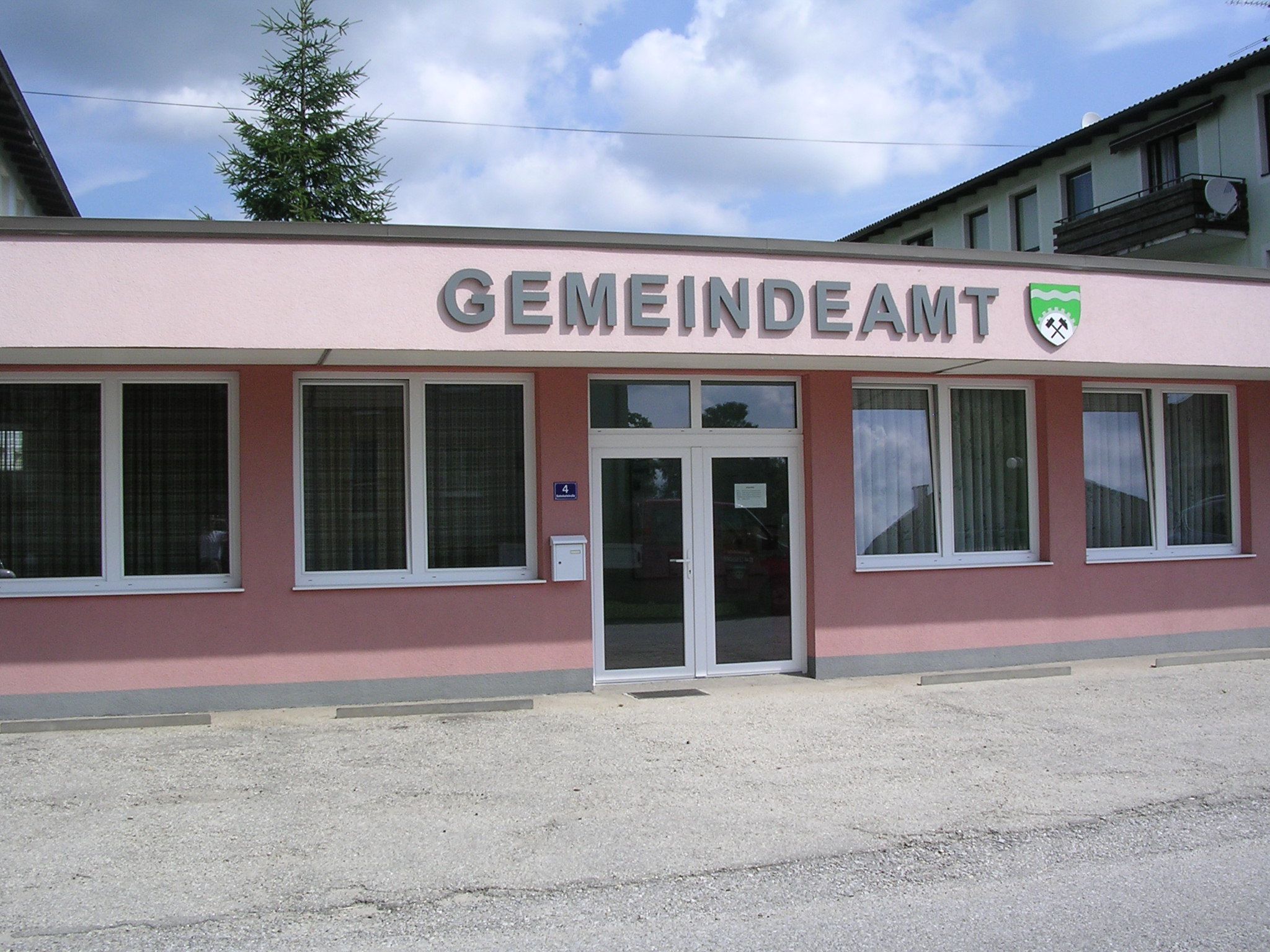Pohľad zvonka na ružovú budovu s nápisom "GEMEINDEAMT" a erbom.