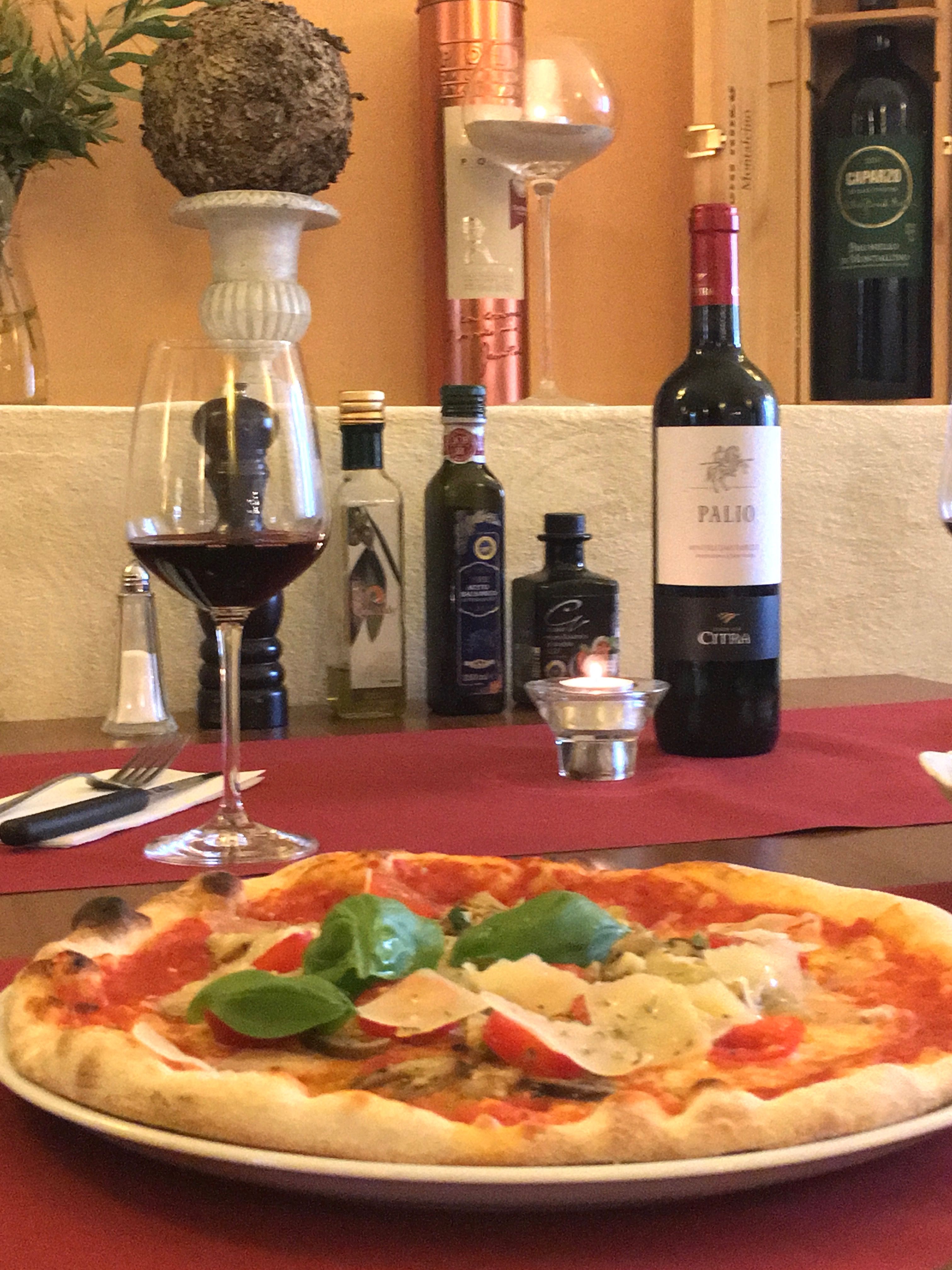 Pizza s bazalkou a parmezánom na stole s červeným vínom a olivovým olejom.