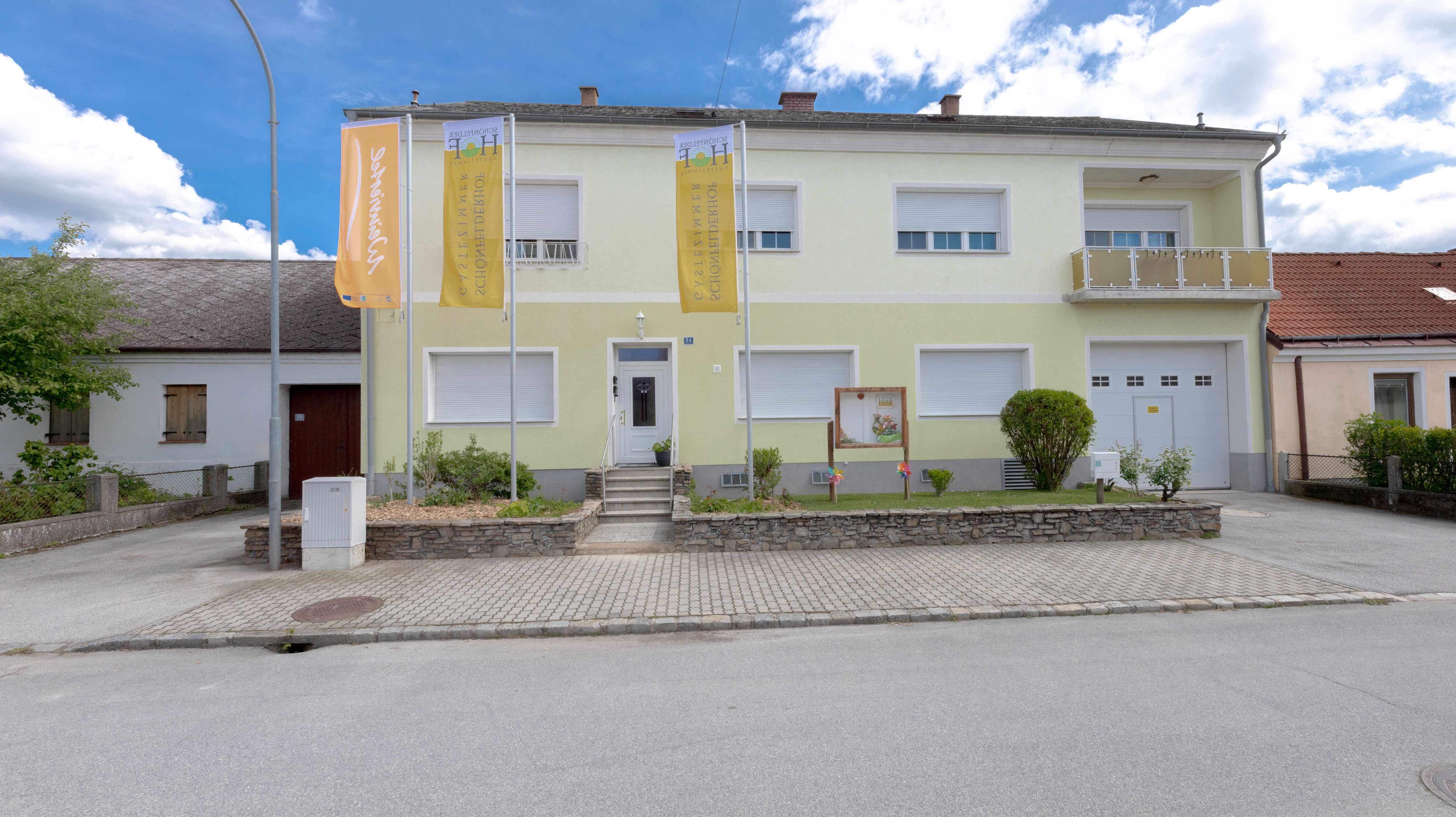 Pohľad zvonku na dvojposchodovú budovu so žltou fasádou a dvoma vlajkami pred ňou.
