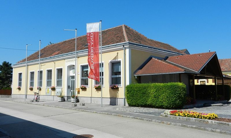 Obecný úrad v Rauchenwarthu, žltá budova s červenou strechou a kvetmi.