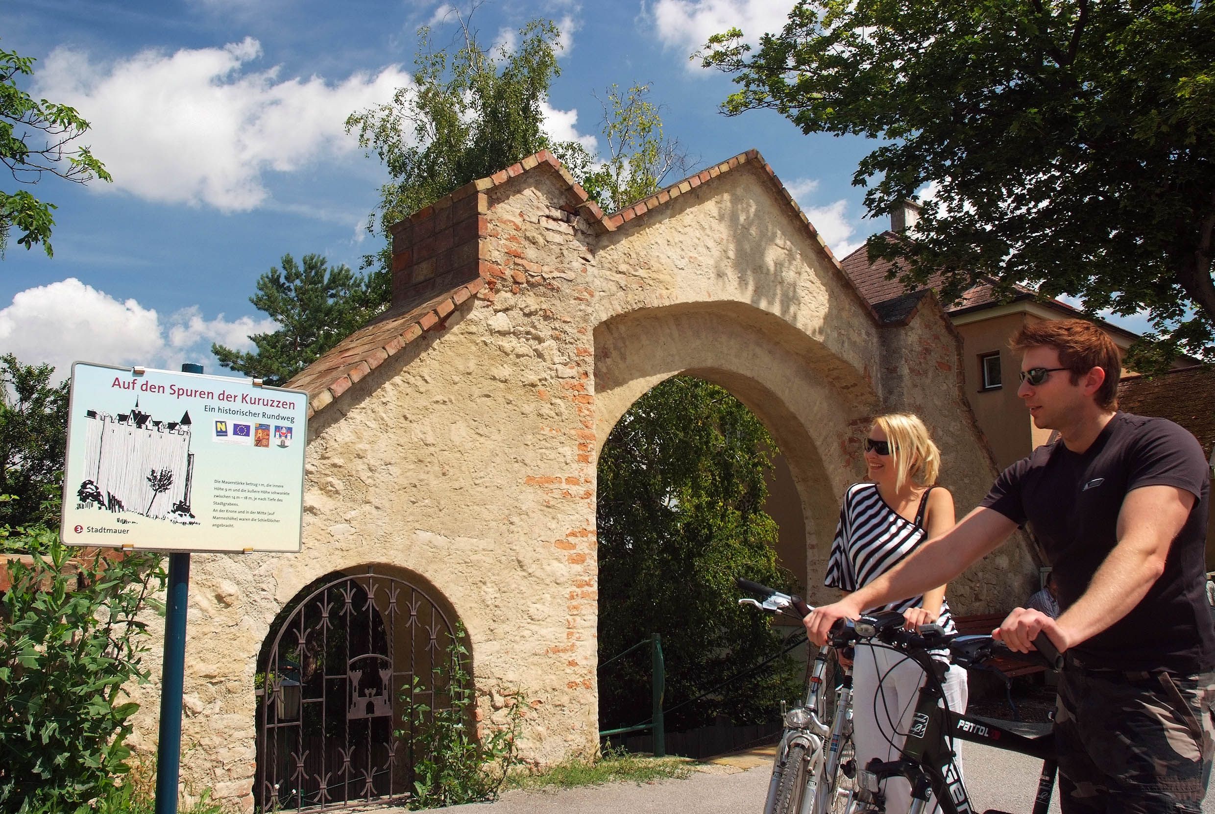 Dvaja ľudia s bicyklami pred historickým oblúkom v Zistersdorfe.