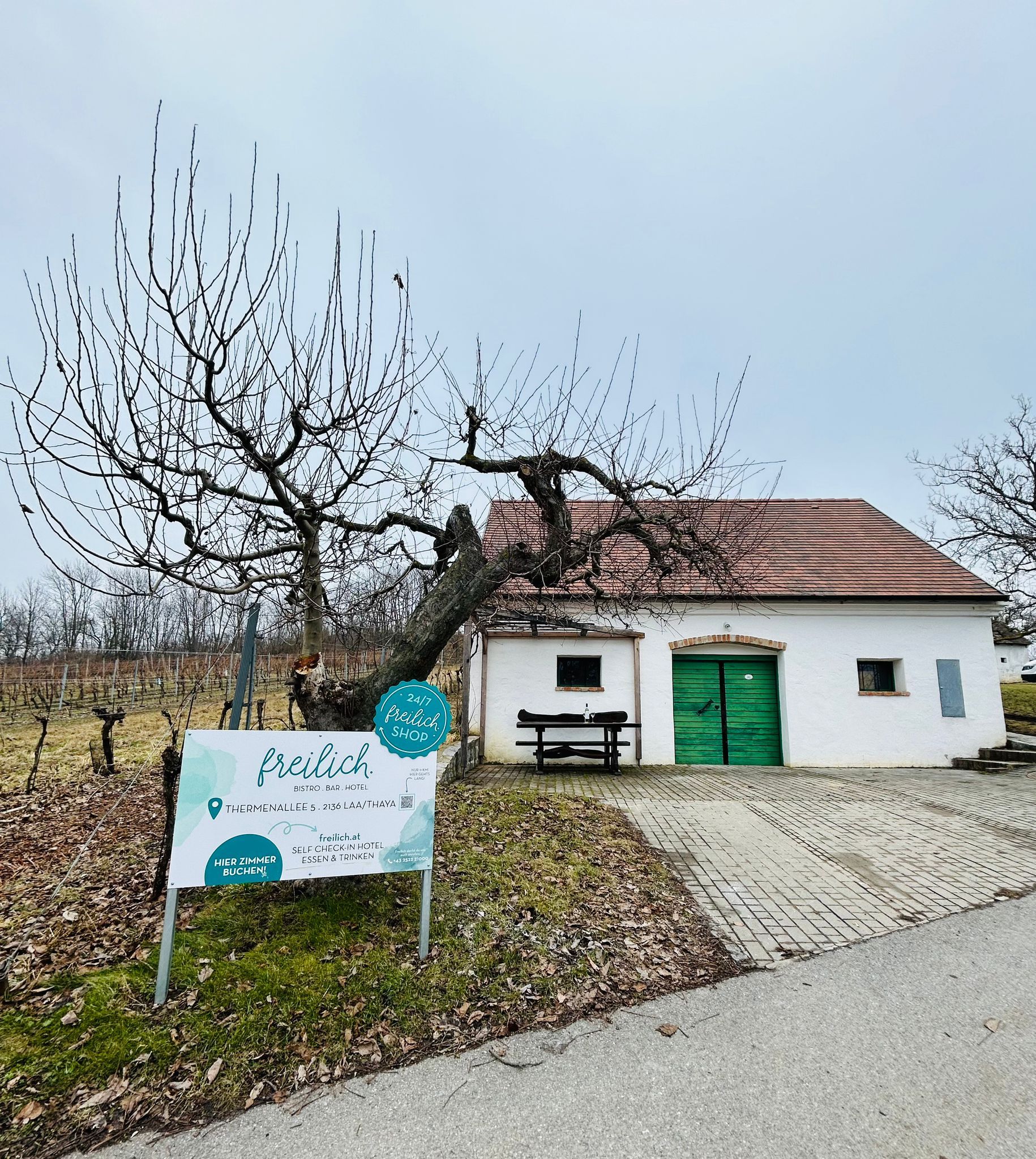 Biela budova so zelenou bránou a nápisom "freilich" vo vidieckom prostredí.