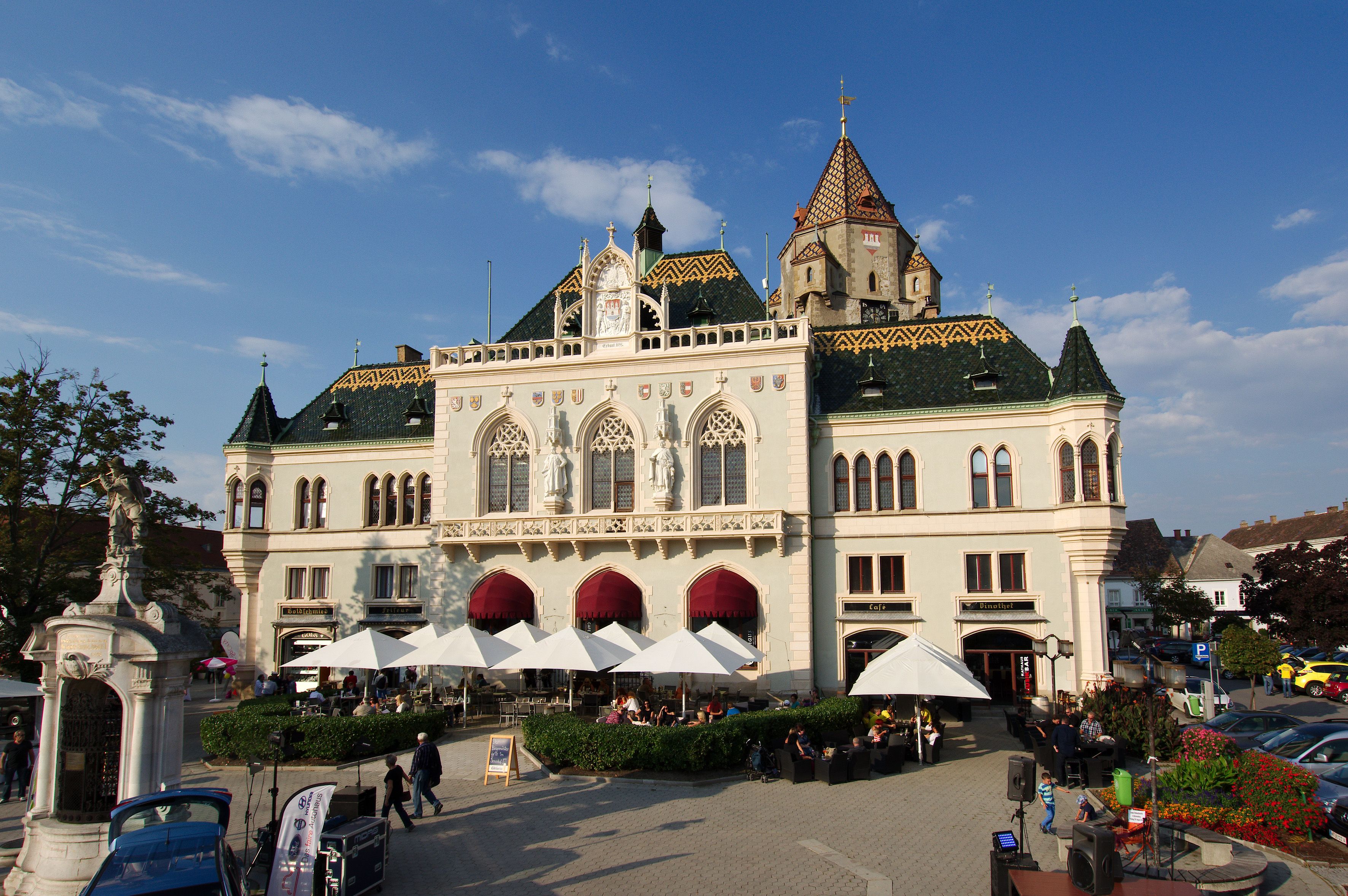 Korneuburská radnica s pozoruhodnou architektúrou a slnečníkmi v popredí.