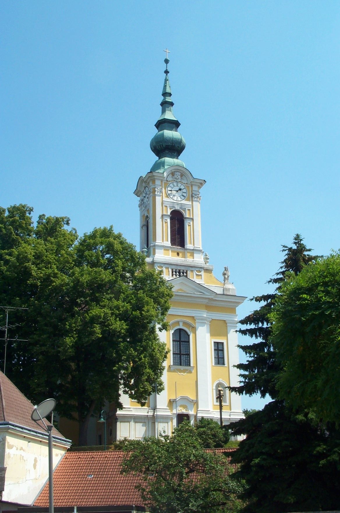 Žltý kostol s vežou a hodinami v Groß-Siegharts, obklopený stromami.