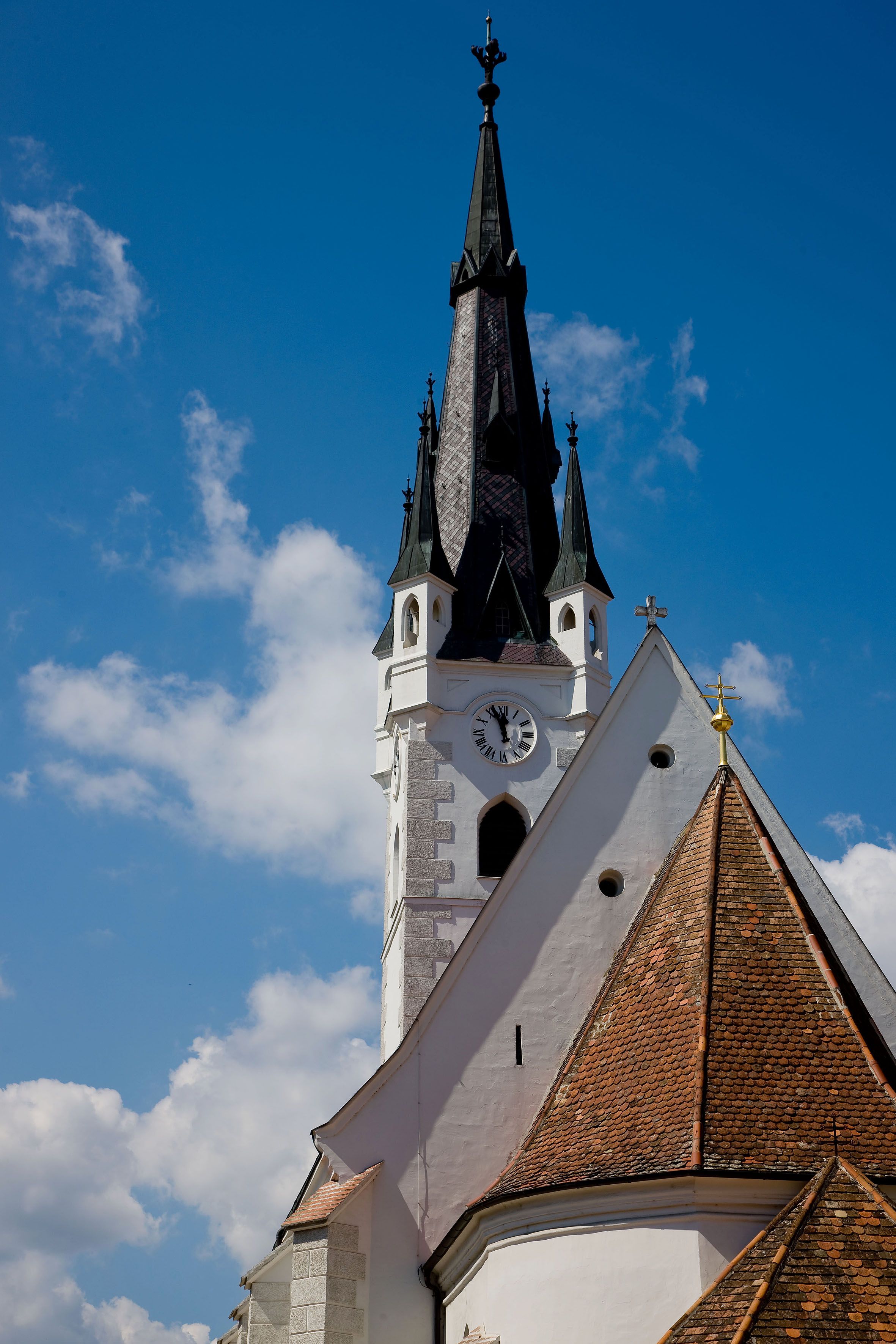 Kostolná veža s hodinami a špicatou strechou na pozadí modrej oblohy.