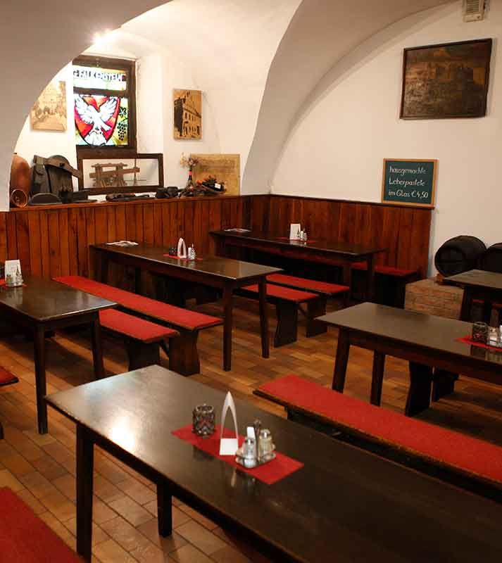 Pohľad do interiéru tradičnej viedenskej krčmy s drevenými stolmi a červenými lavicami.