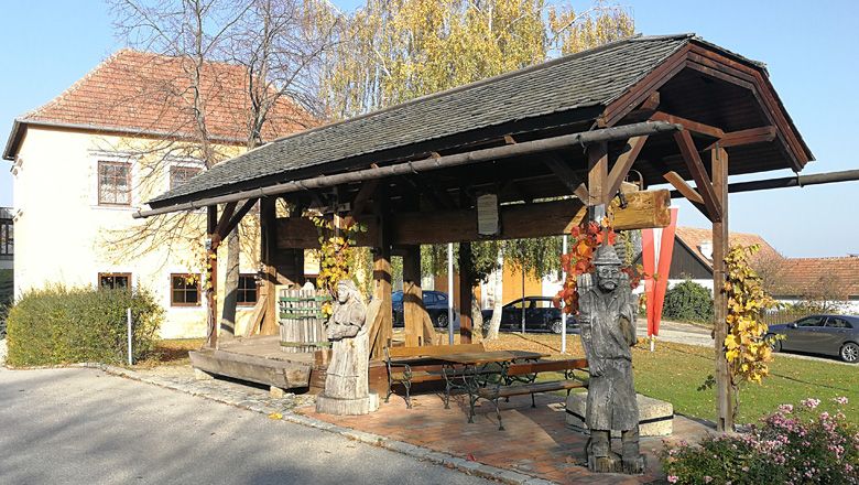 Historický lis na stromy s drevenými figúrkami v Drosse, obklopený jesennou vegetáciou.