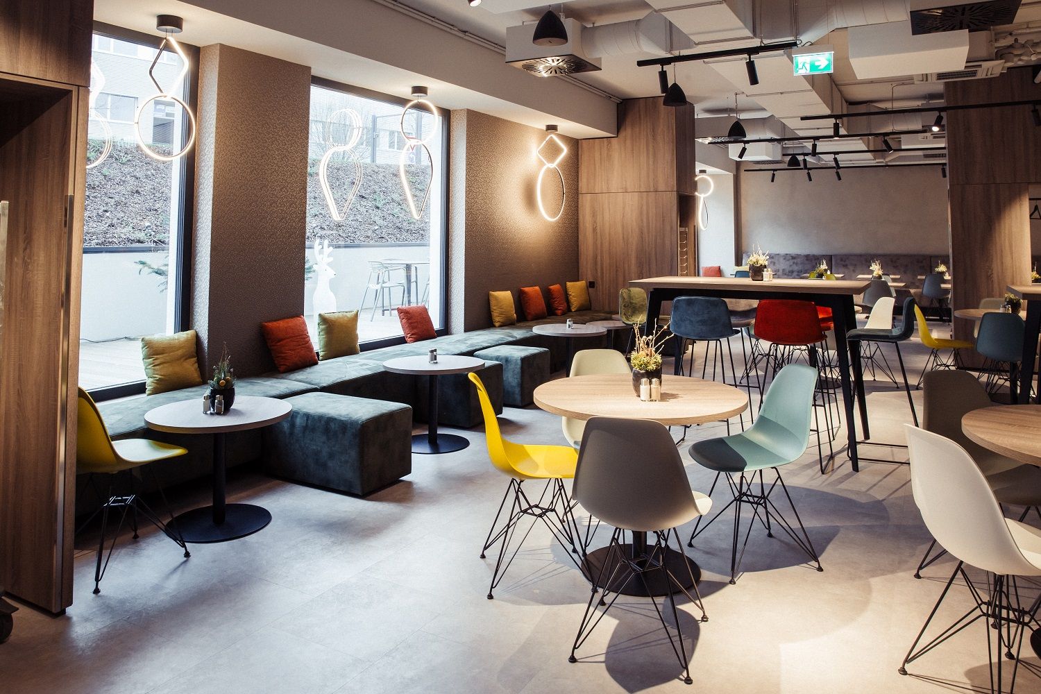 Moderná hotelová reštaurácia s farebnými stoličkami a stolmi, veľkými oknami a štýlovým osvetlením.