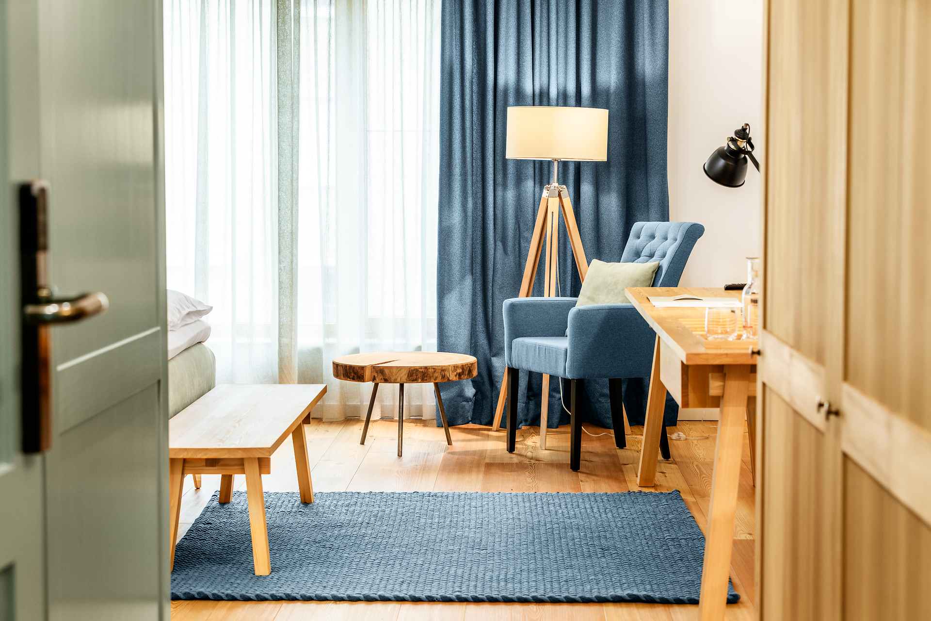 In einem stilvoll eingerichteten Raum mit sanften Farben und warmem Licht lädt ein bequemer Sessel zum Entspannen ein. Die großen Fenster lassen viel Tageslicht herein und bieten einen Blick auf die ruhige Umgebung, während der Holzfußboden eine gemütliche Atmosphäre schafft.