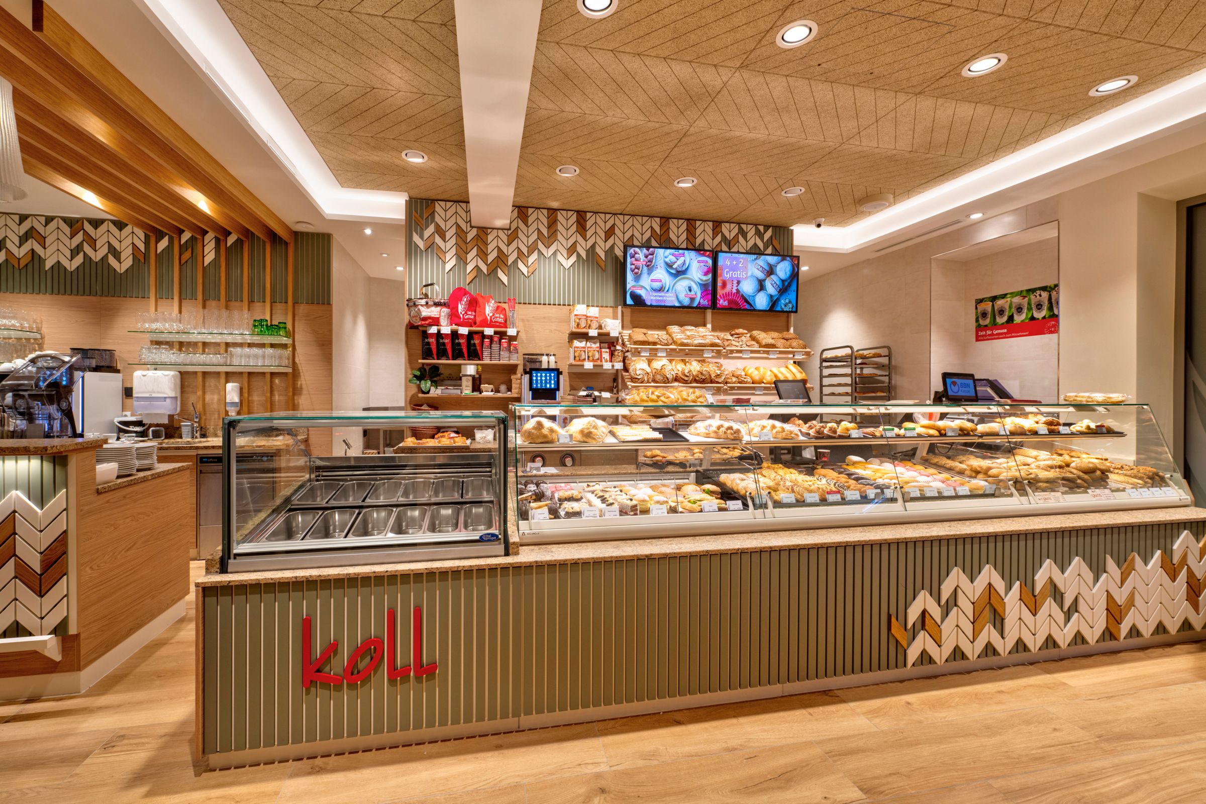 Pohľad do interiéru modernej pekárne s pultom plným pečiva a kávovarom.