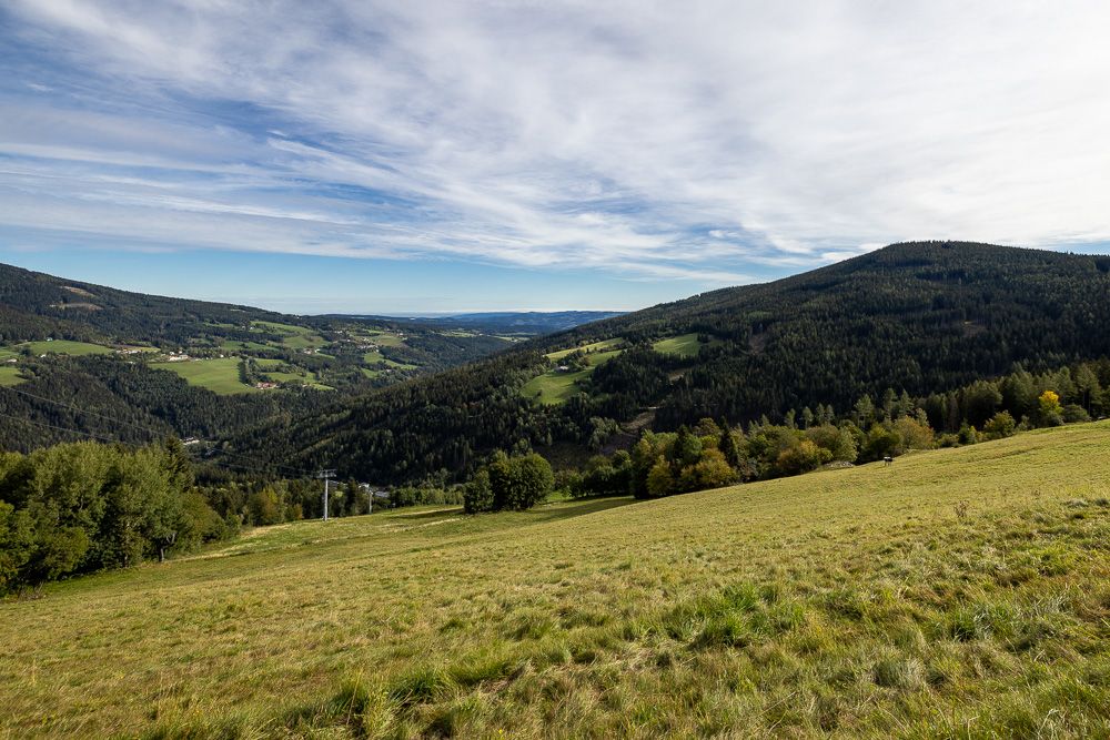 Rozsiahla zelená krajina s kopcami a lesmi pod zamračenou oblohou.