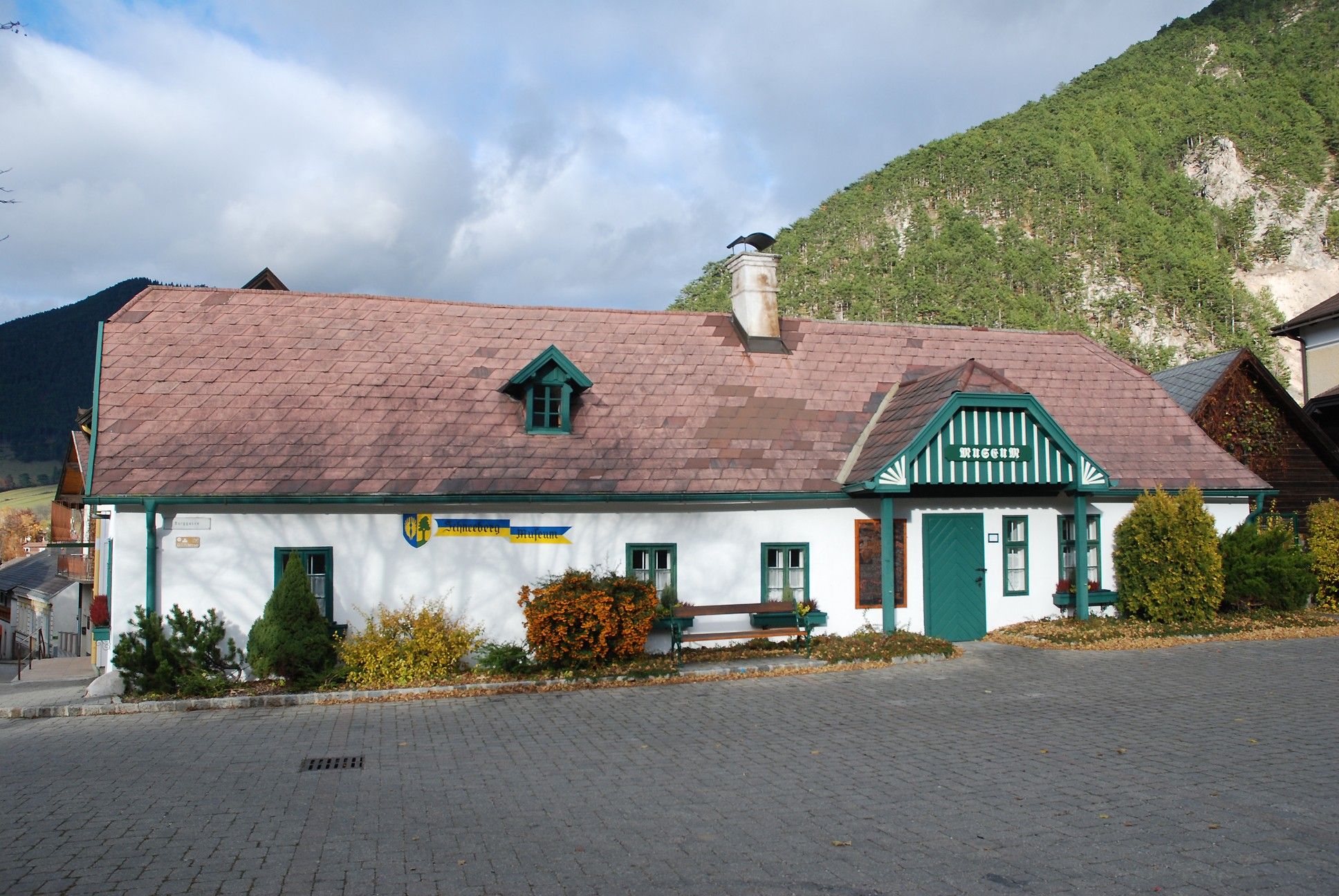 Schneeberg Museum Puchberg, tradičná budova so zelenou strechou a komínom, obklopená horami a stromami.