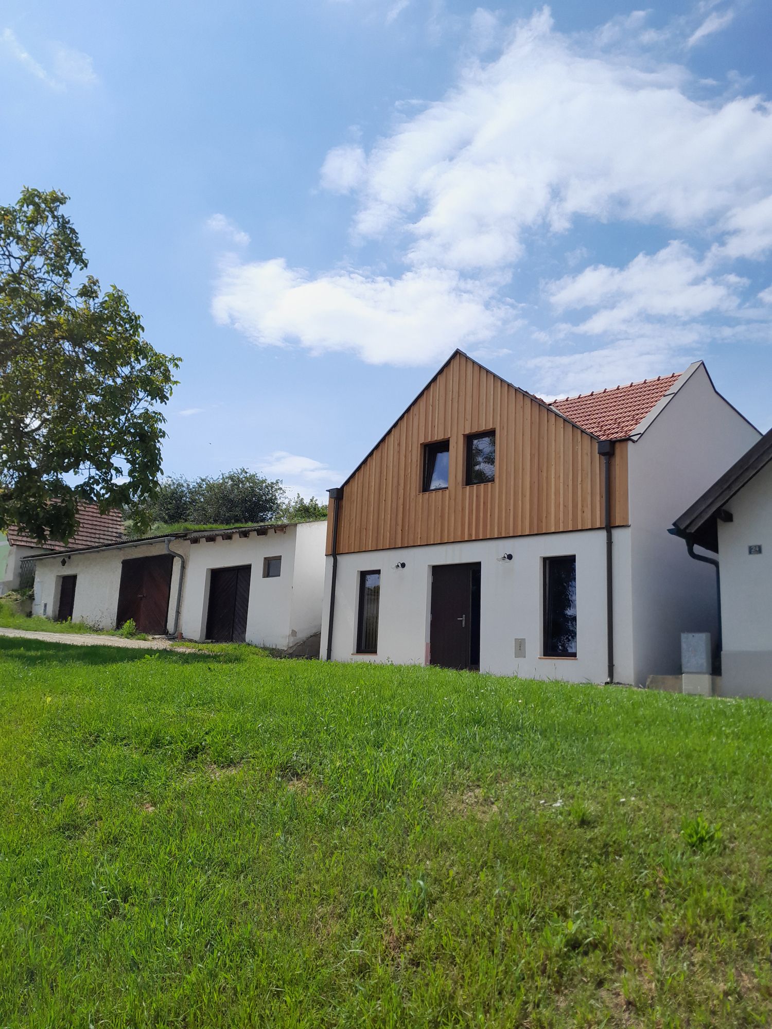 Na zelenom kopci pod modrou oblohou stojí moderná budova s drevenou fasádou a červenými škridlami.
