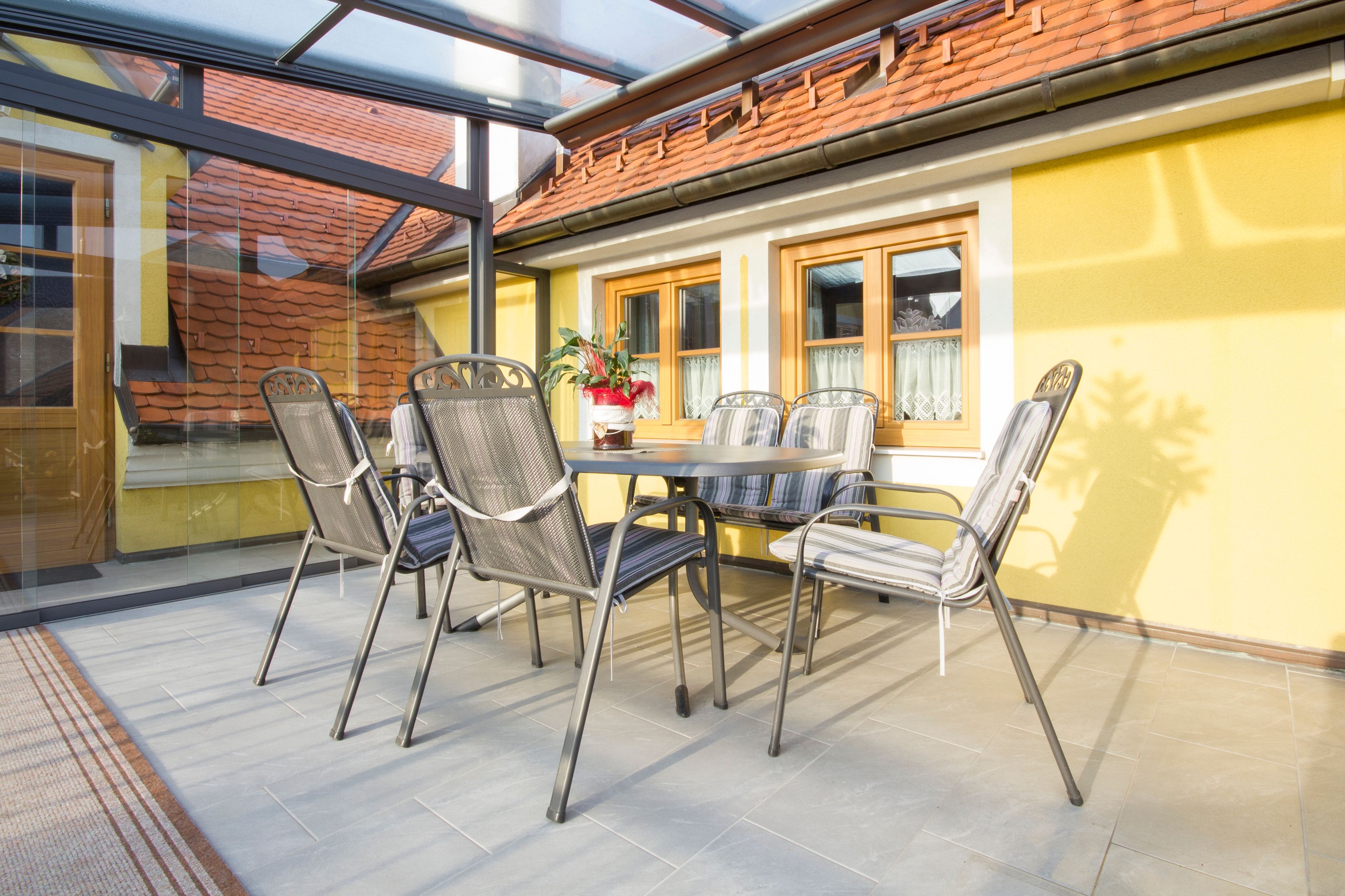 Zimná záhrada so stolom a stoličkami, žlté steny, sklenená strecha.