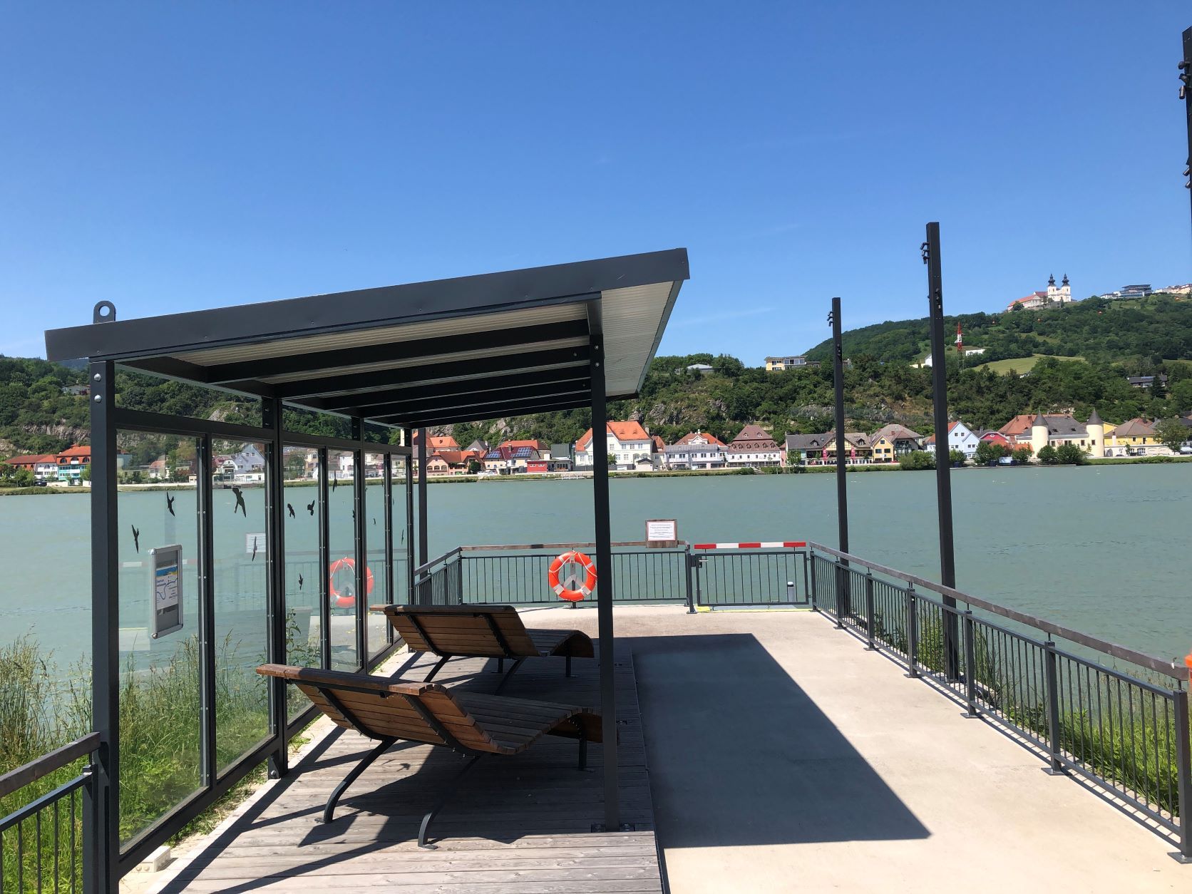 Kotvisko s baldachýnom a ležadlami, rieka v pozadí, bazilika na kopci.