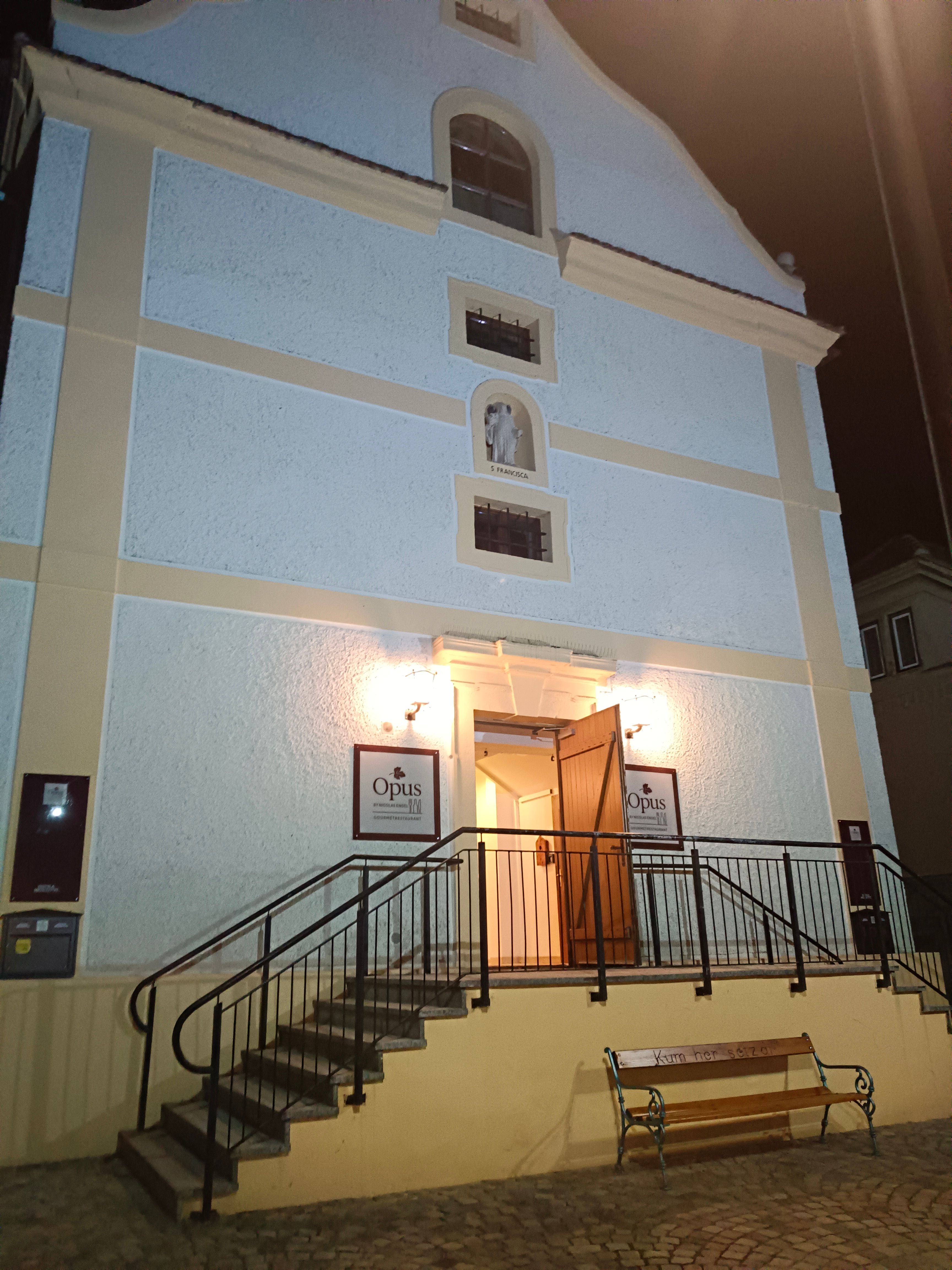 Vchod do budovy so schodmi a otvorenými dverami, osvetlený v noci.