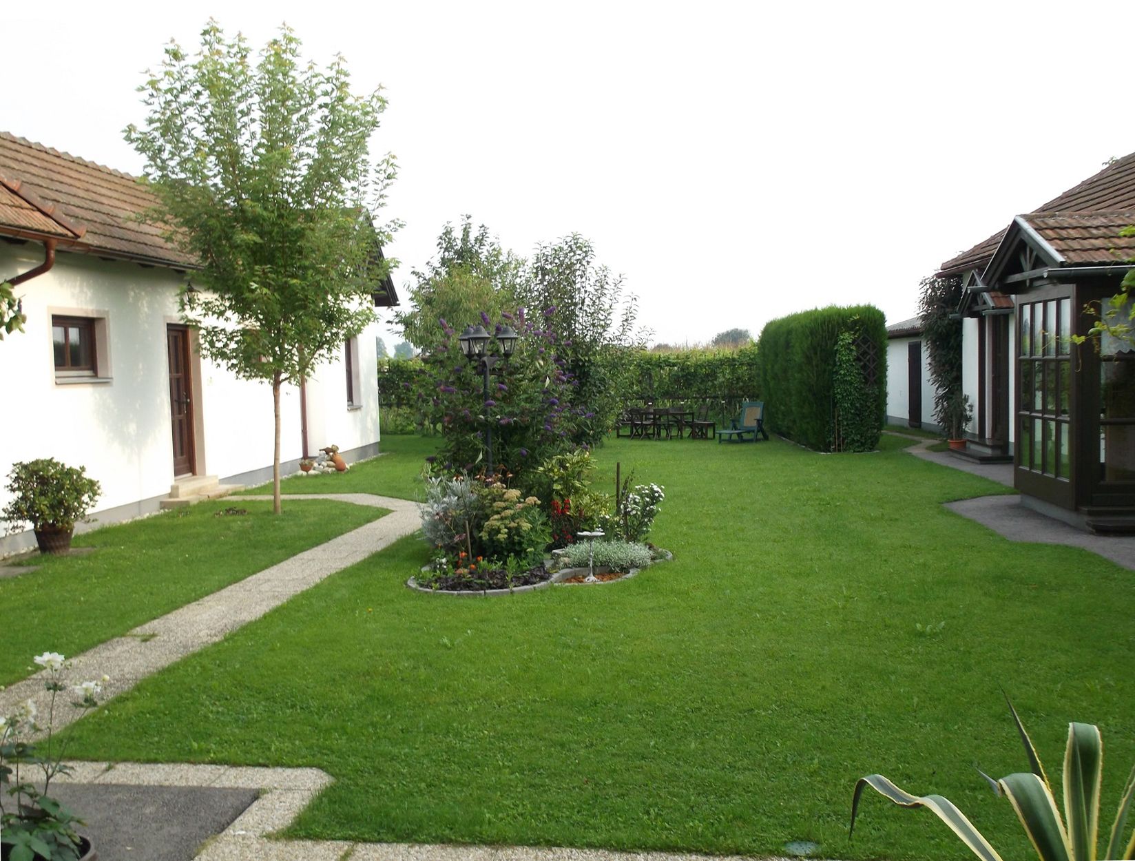 Veľmi dobre udržiavaná záhrada s výhľadom na kríky a stromy, s časťou budovy v pozadí.