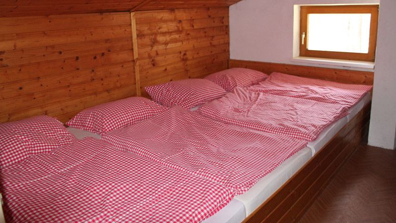 Tri postele s červenými a bielymi šachovnicovými perinami v izbe obloženej drevom.