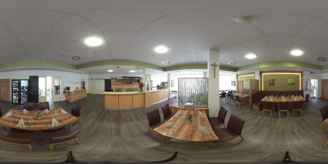 Pohľad do interiéru modernej reštaurácie s drevenými stolmi a stoličkami, zdobenej rastlinami a umeleckými dielami na stenách.