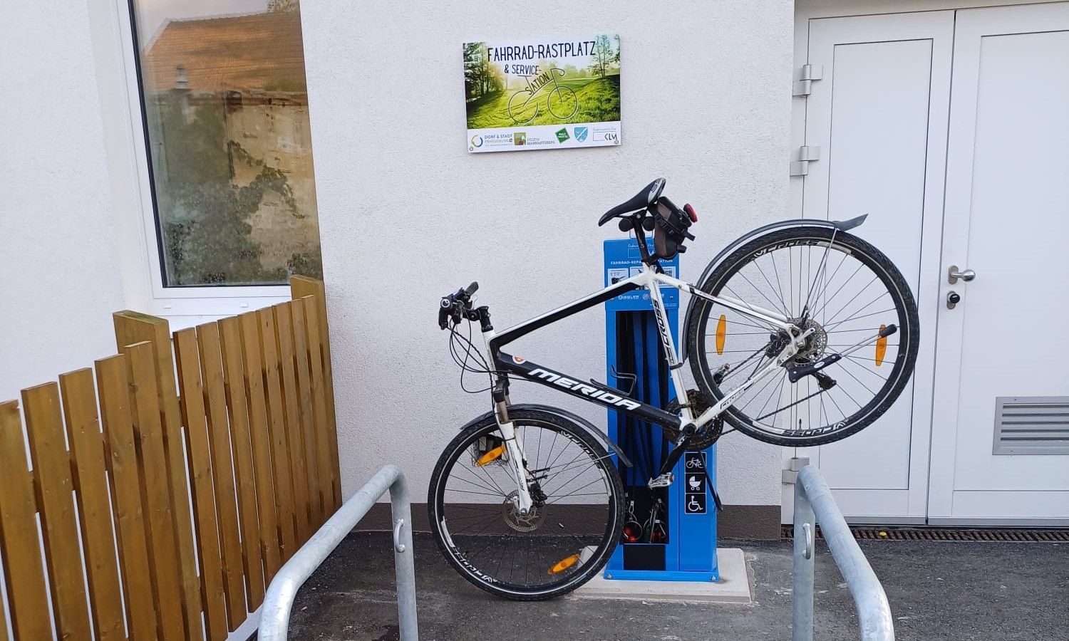 Bicykel zamknutý na modrej čerpacej stanici vedľa budovy s nápisom "Bicycle Rest Area & Service Station".
