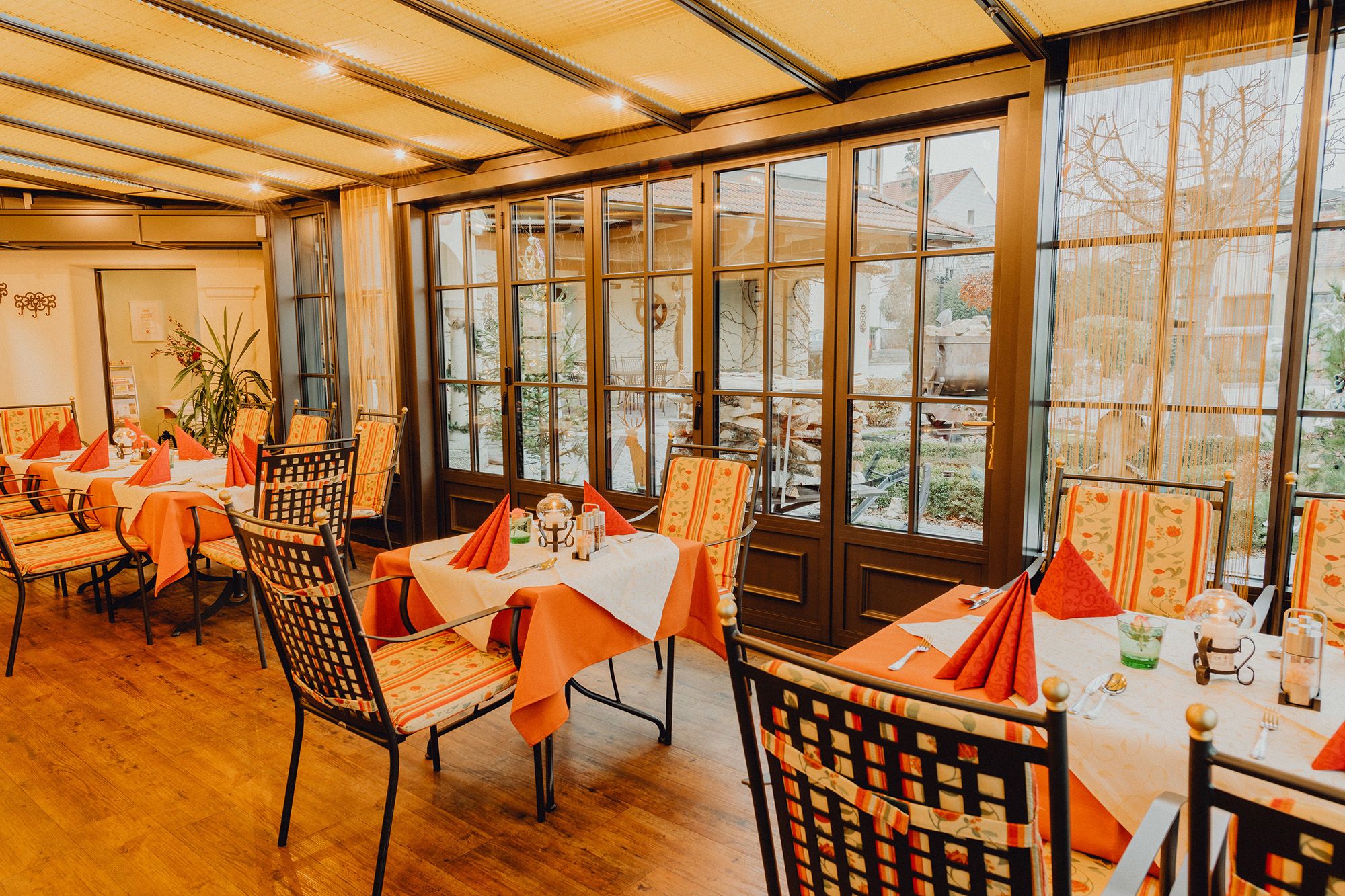 Útulná zimná záhrada so stolmi a stoličkami, obklopená veľkými oknami s výhľadom von.