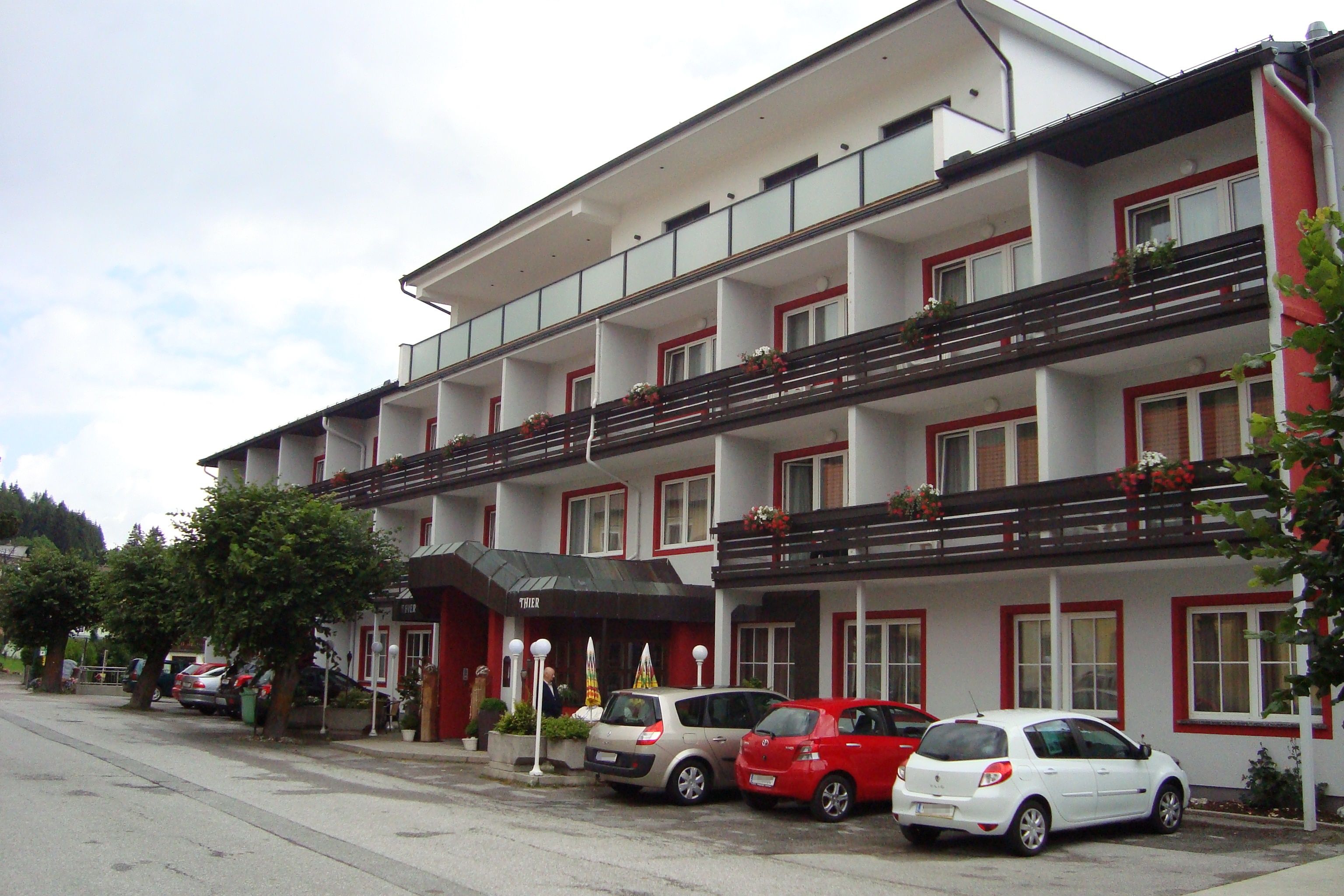 Exteriérový pohľad na hotel Thier so zaparkovanými autami a balkónmi s kvetmi.