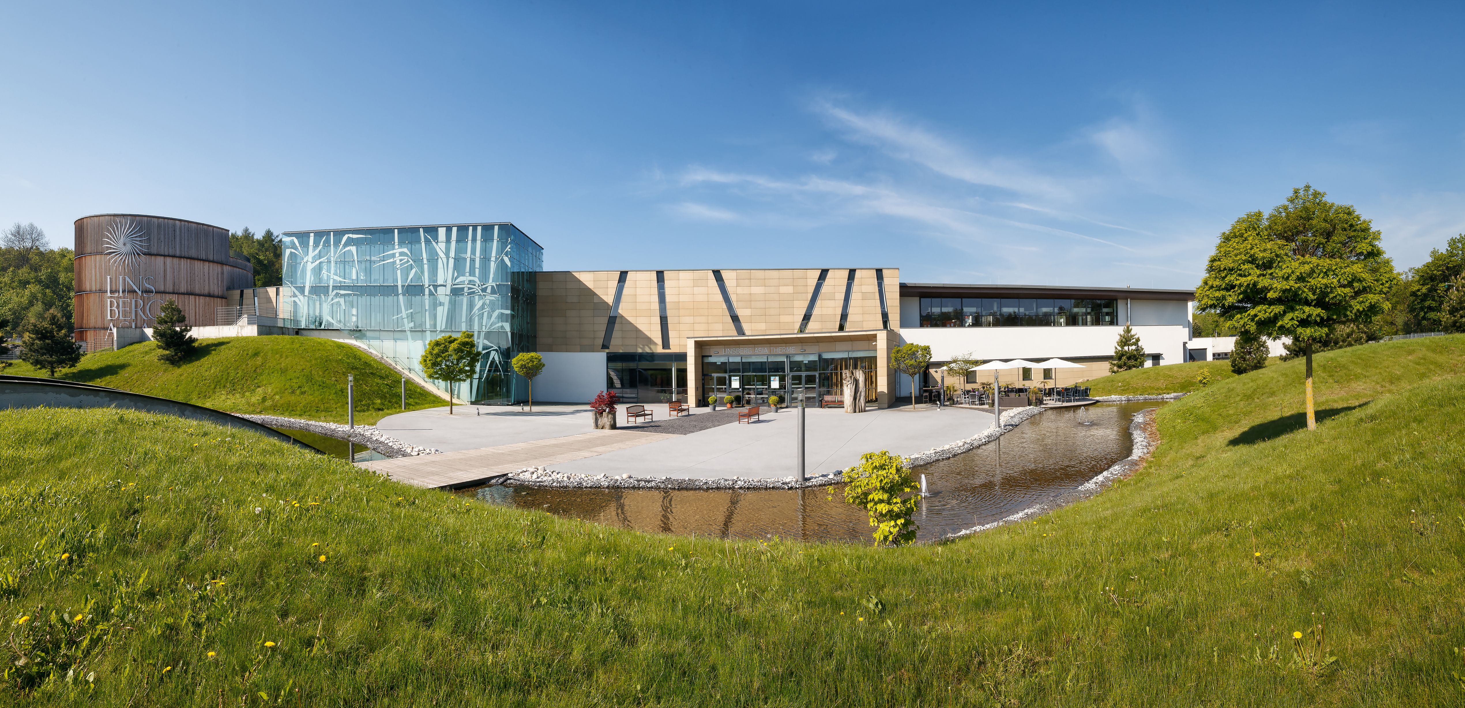 Exteriérový pohľad na kúpele Linsberg Asia Therme s modernou architektúrou a zelenými plochami.