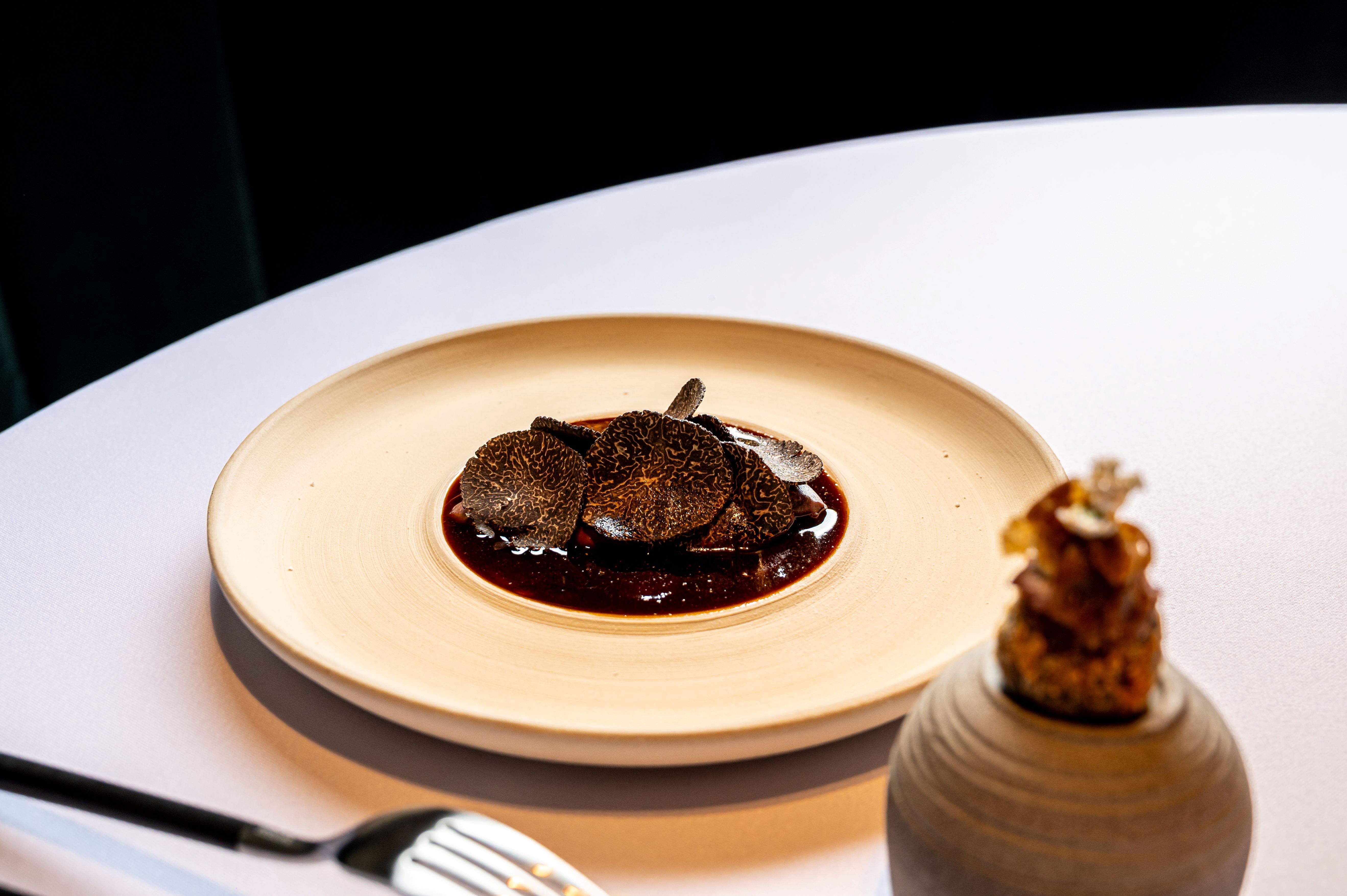 Gurmánsky pokrm s plátkami hľuzoviek na tanieri s ozdobným prvkom vedľa.