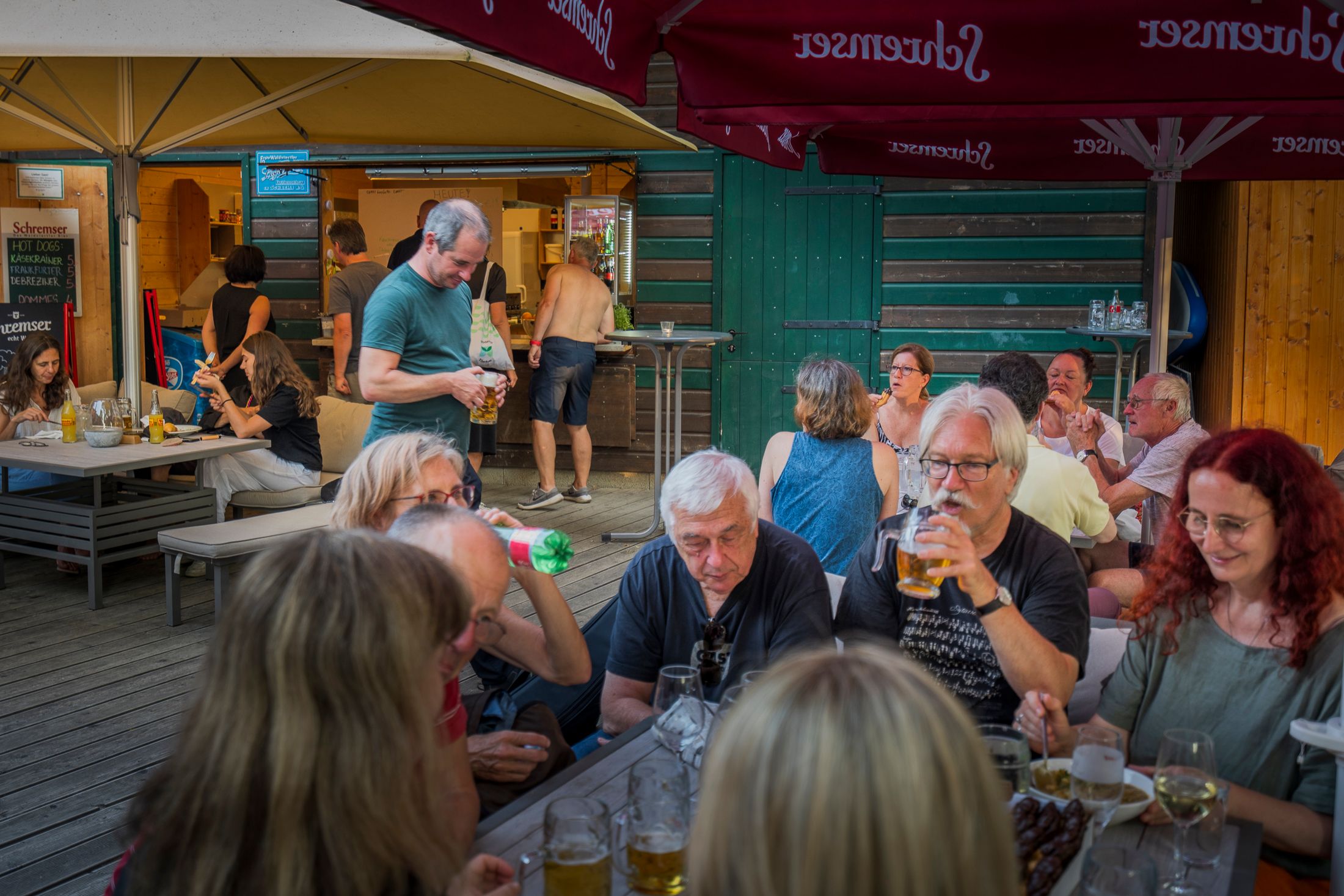 Ľudia sedia pri stoloch v pivnej záhrade a vychutnávajú si nápoje a občerstvenie.