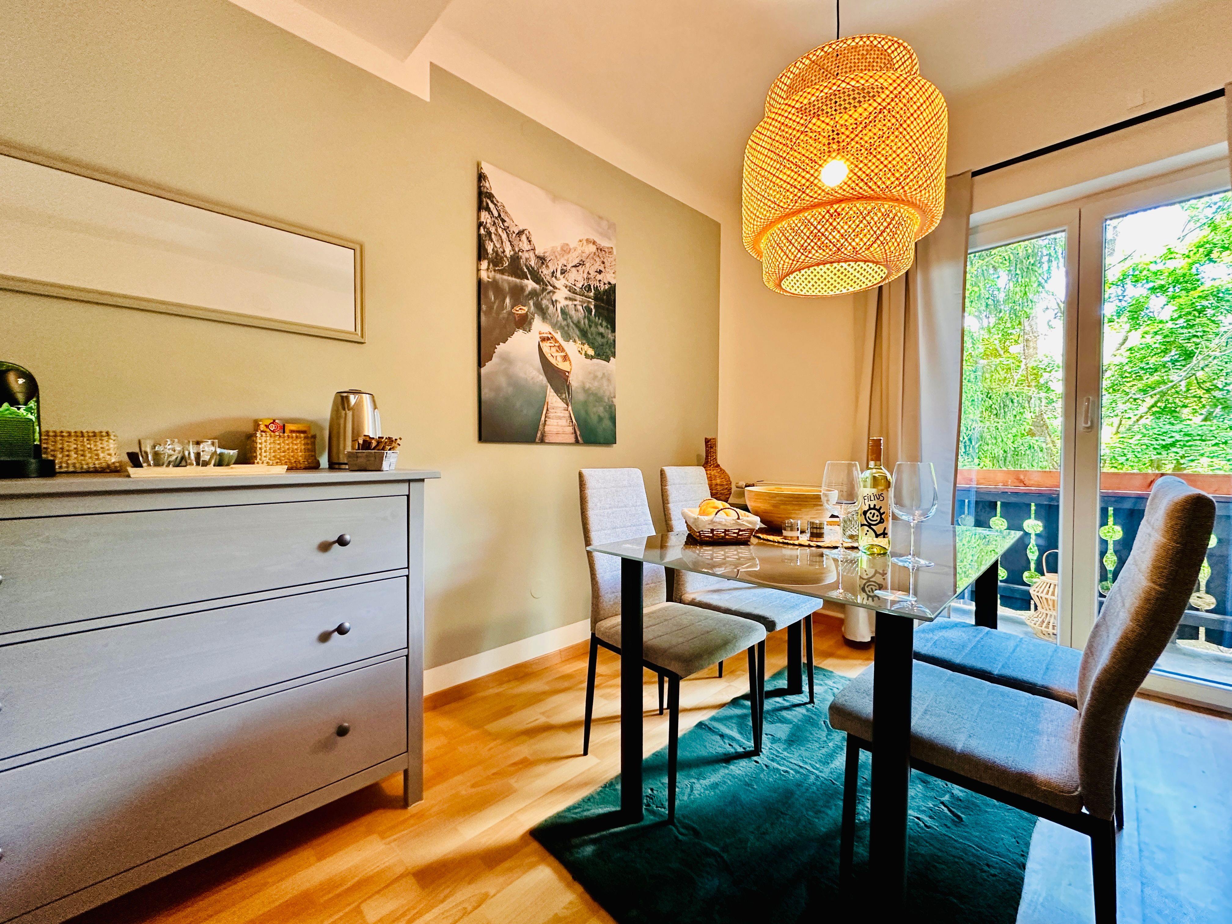 Útulná jedáleň so stolom, stoličkami a závesnou lampou, výhľad na balkón a prírodu.