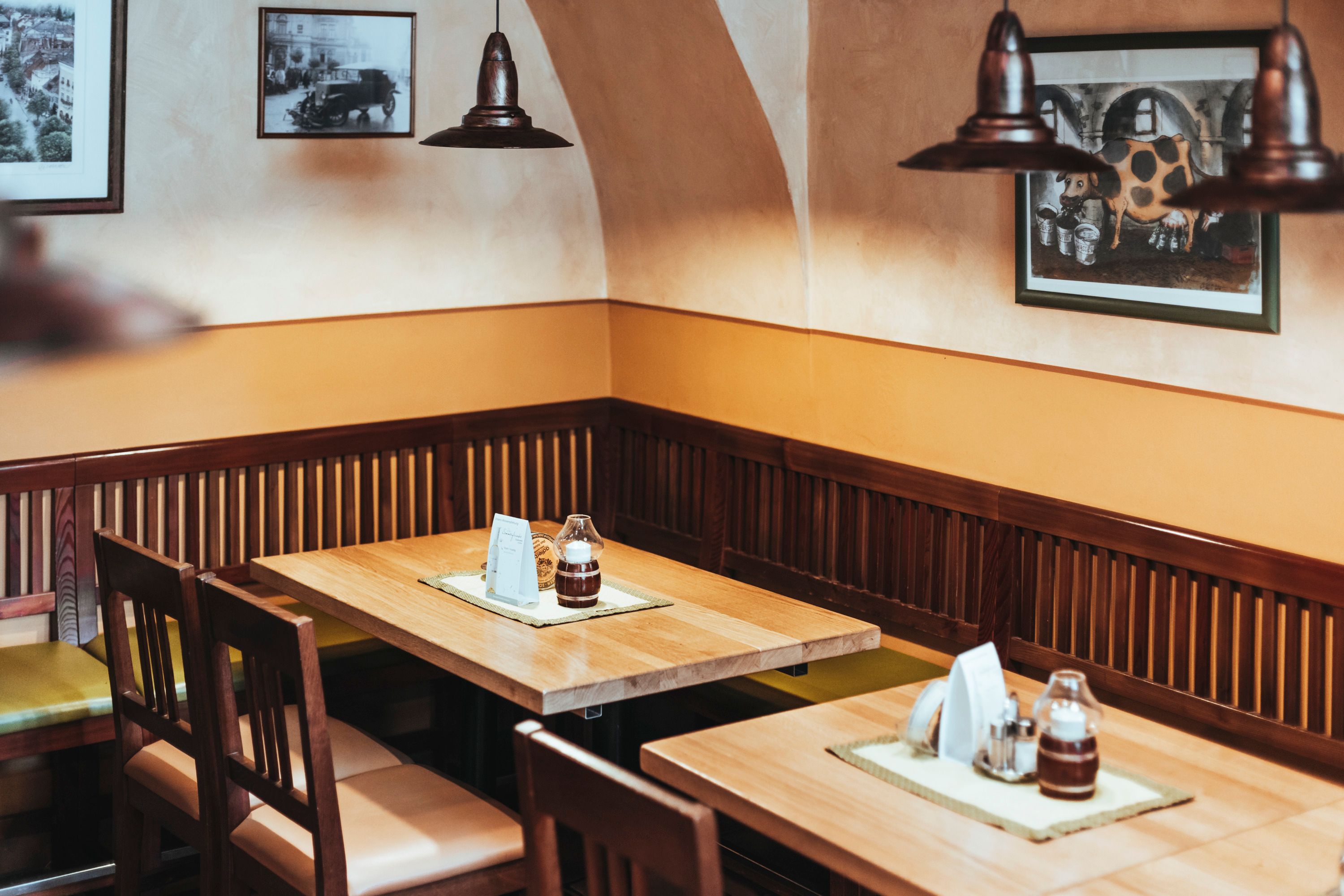 Útulné posedenie v reštaurácii s drevenými stolmi a stoličkami, zdobené obrazmi na stene.