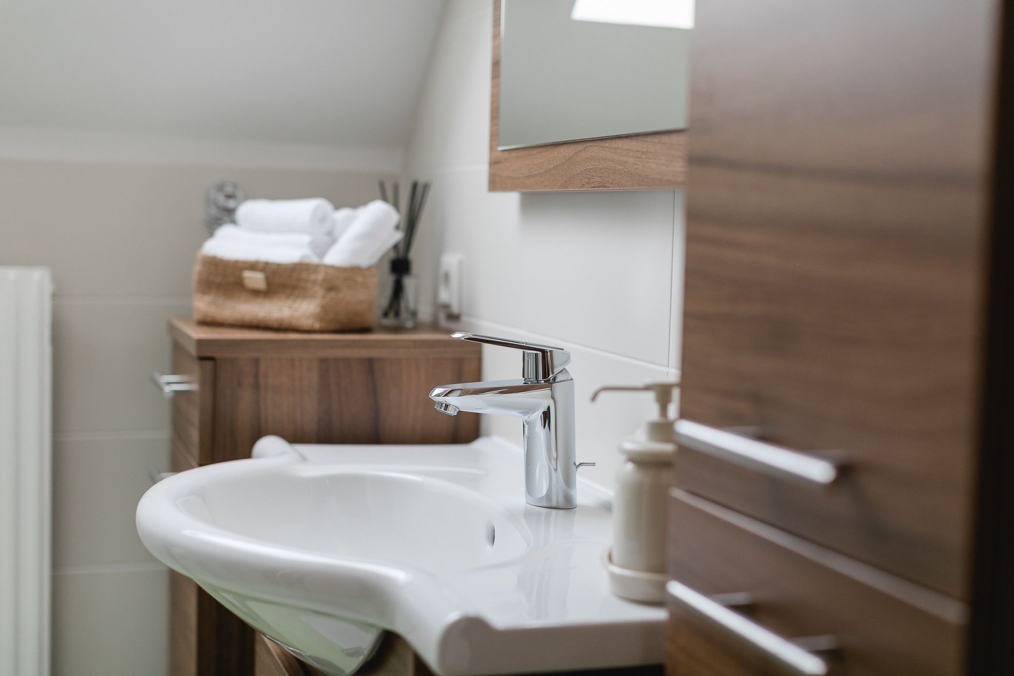 Moderná kúpeľňa s umývadlom, drevenými skrinkami a uterákmi v koši.