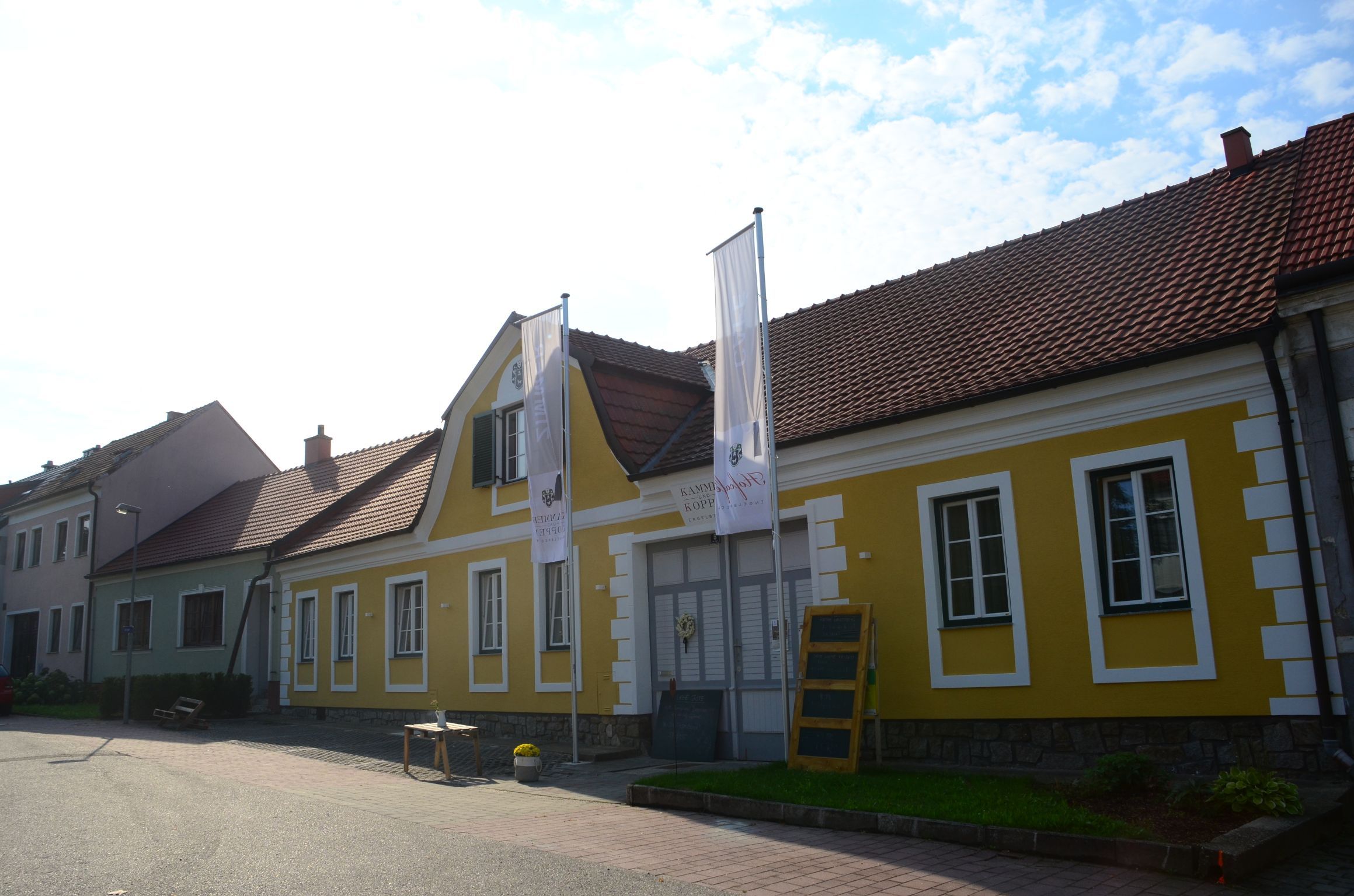 Žltá budova s červenými škridlami a dvoma vlajkami pred ňou.