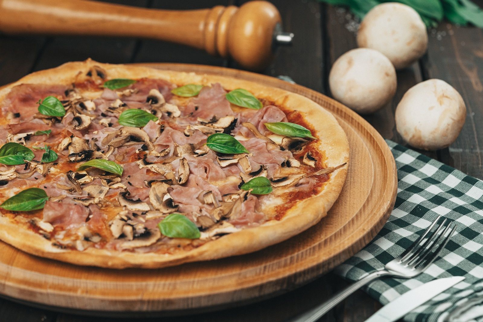 Pizza so šunkou, hubami a bazalkou na drevenej doske.
